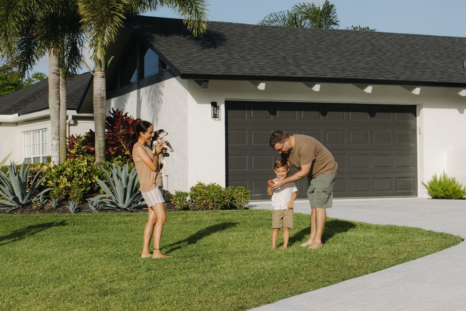 Family playing with their dog in front yard of suburban home.