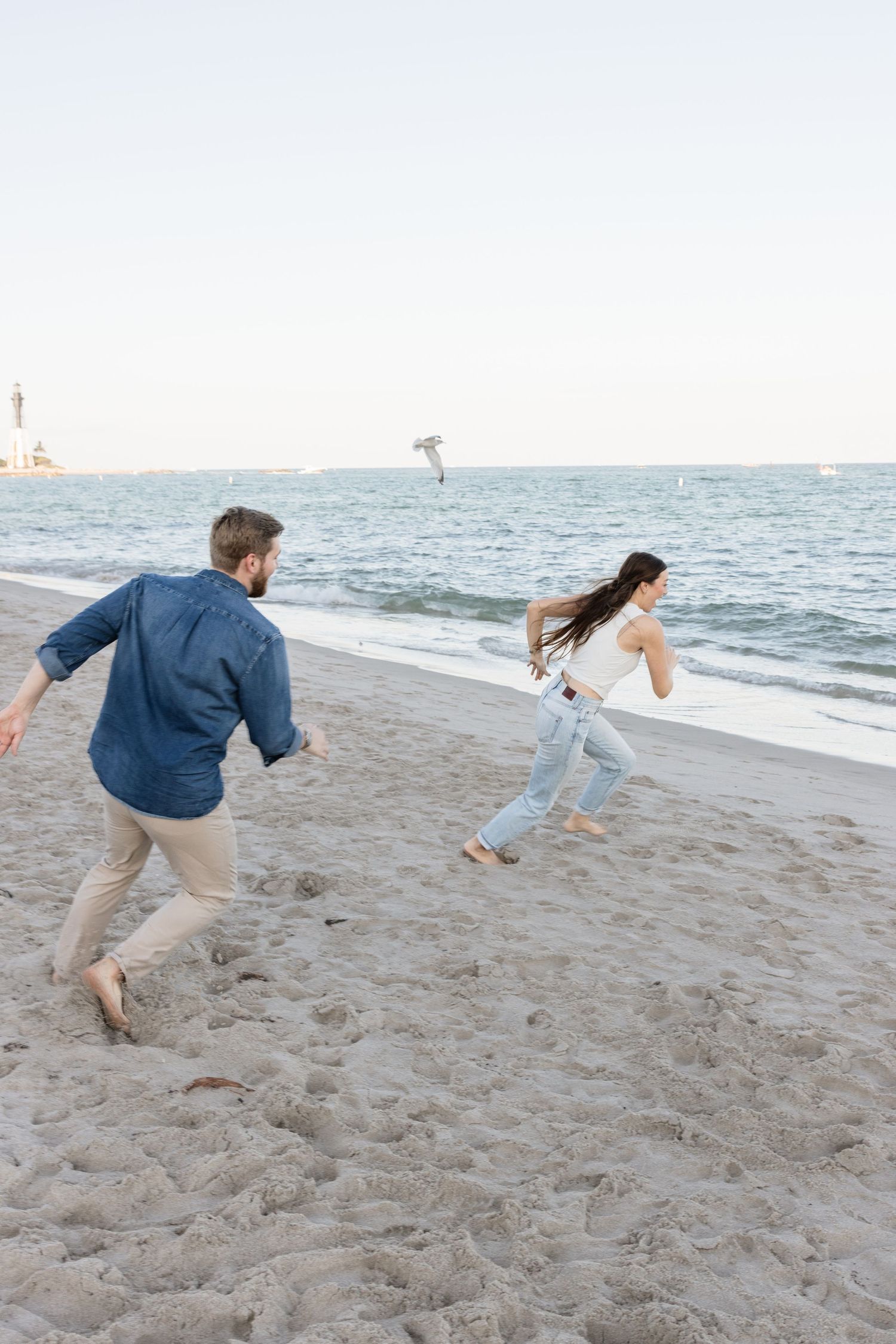 Couple running and playing together on a beach with ocean waves in the background.