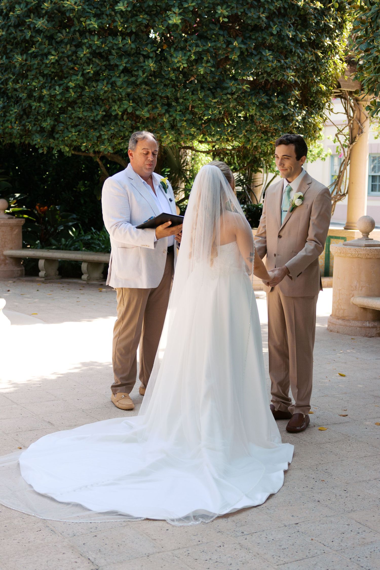 Bride and groom exchanging vows with officiant in an outdoor garden wedding ceremony.