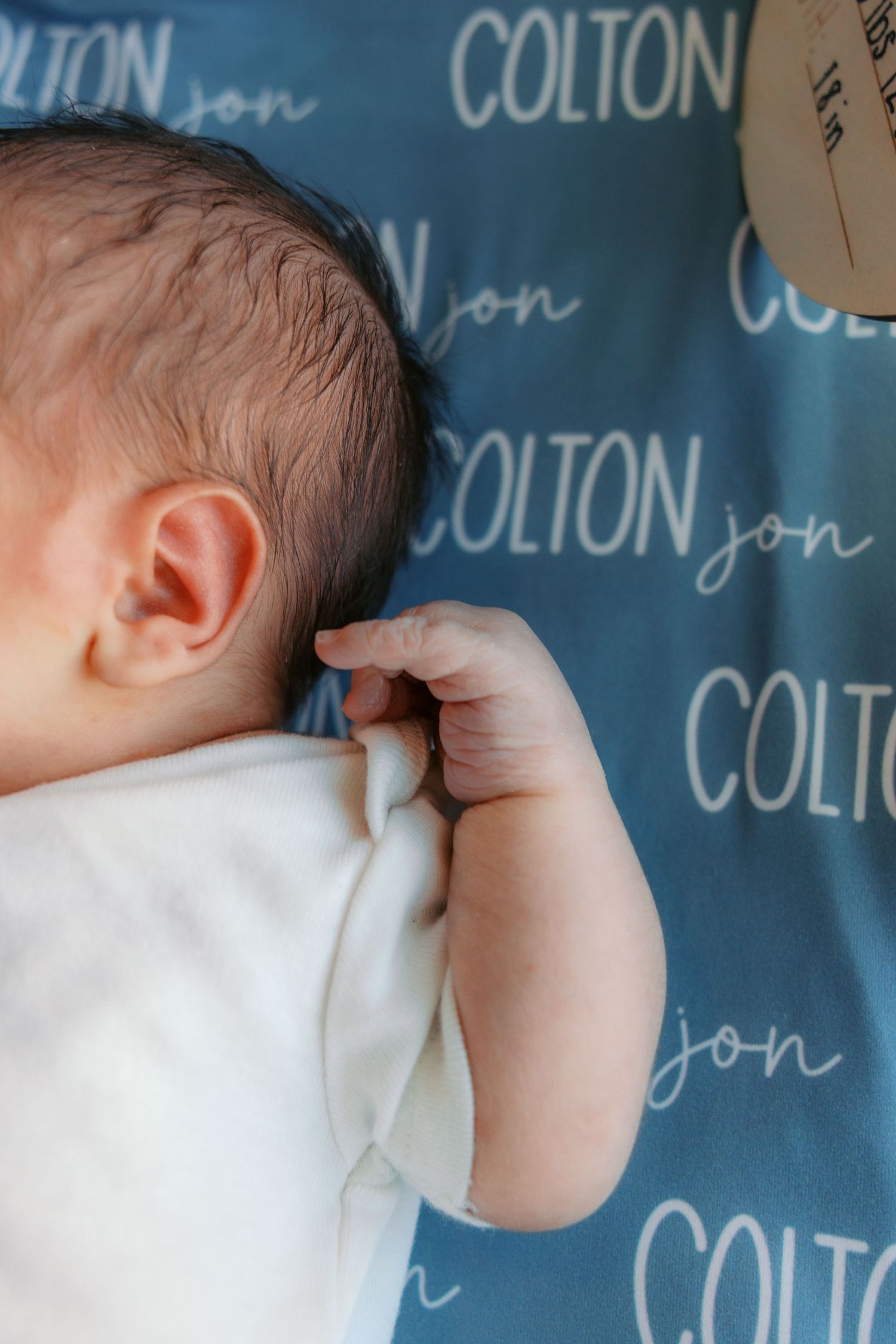 Newborn baby lying on a personalized blue blanket with the name Colton Jon printed in white text.