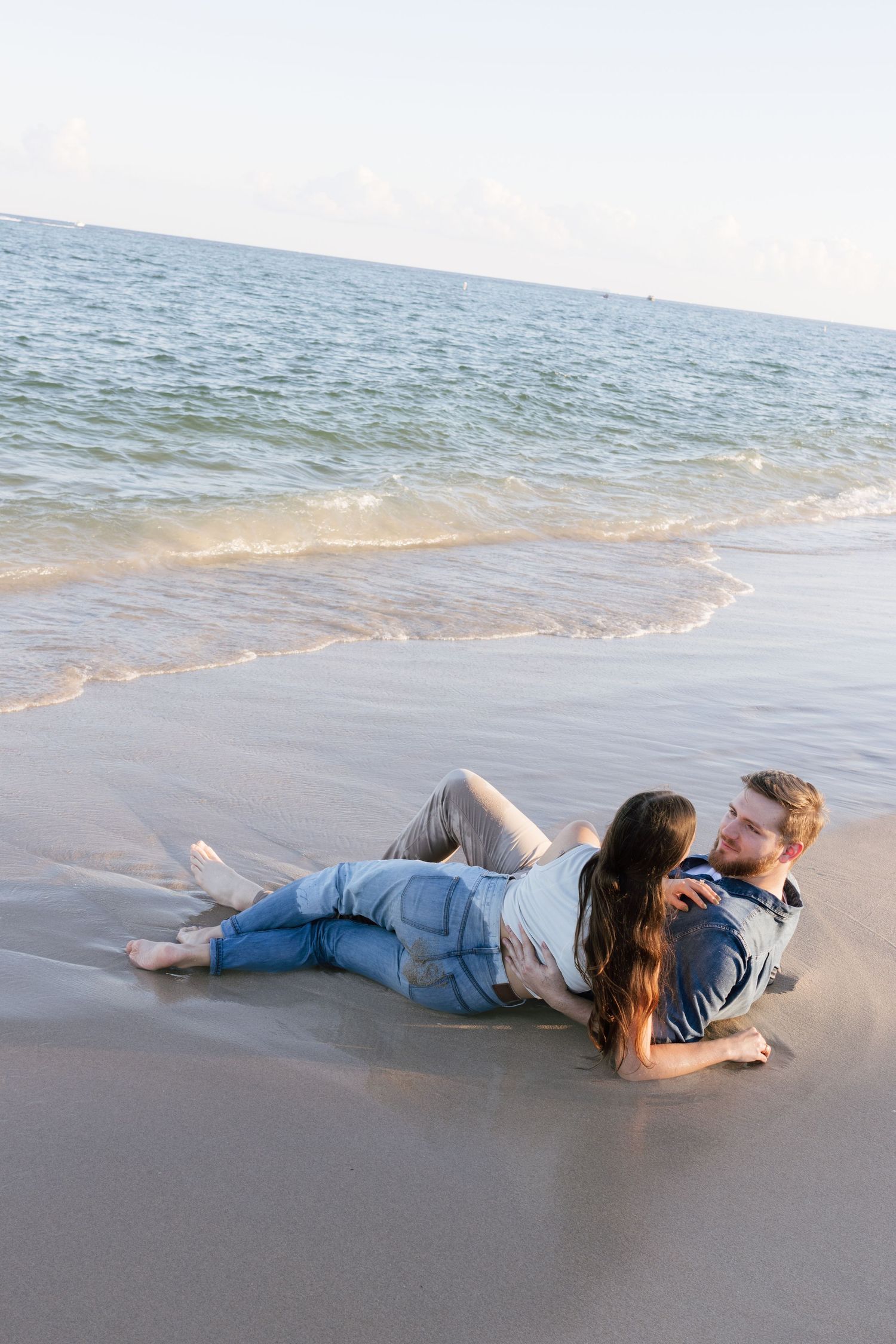 Couple lying together on wet sand as ocean waves approach.