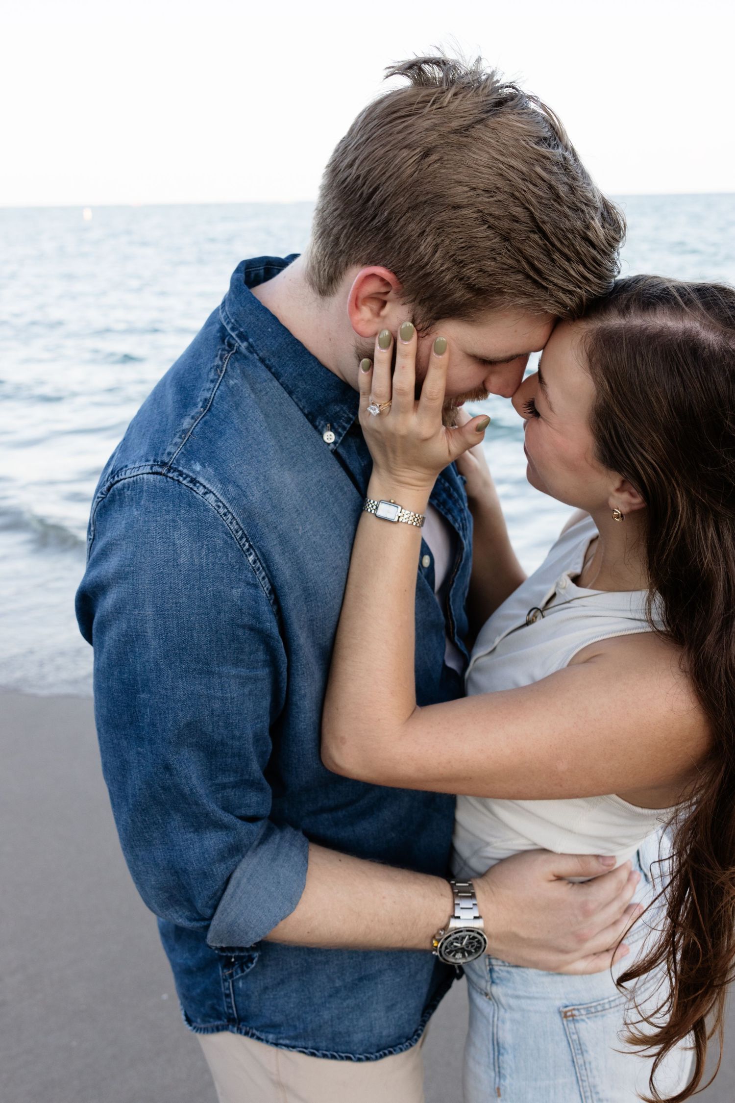 Romantic embrace on the beach with couple in casual denim and white clothing.