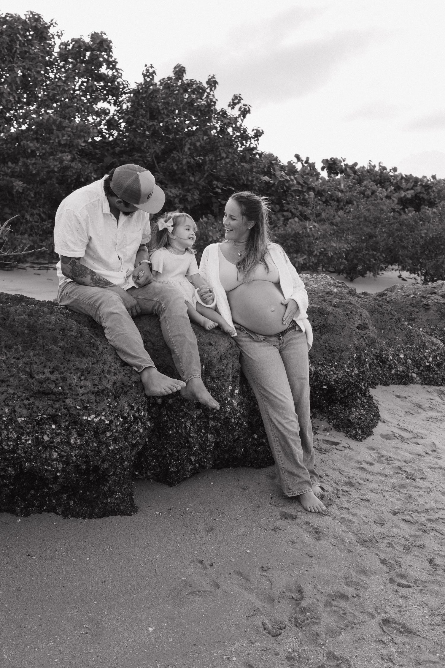 A family sits together on a rocky beach ledge during a casual outdoor photo session.