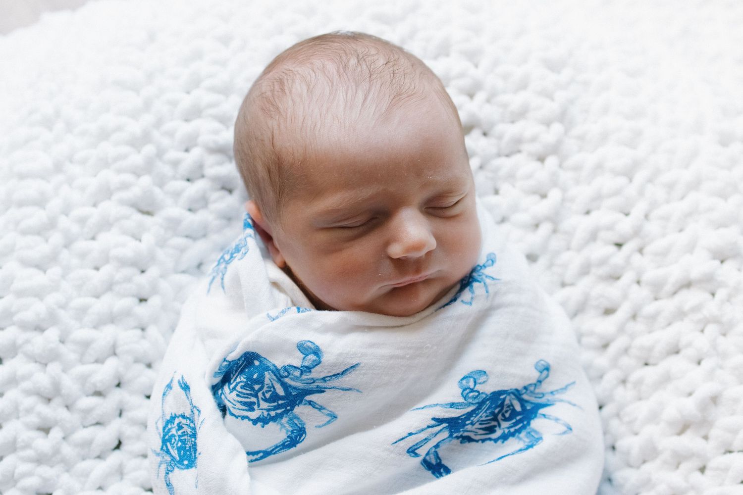 Newborn baby sleeping peacefully on white textured blanket.