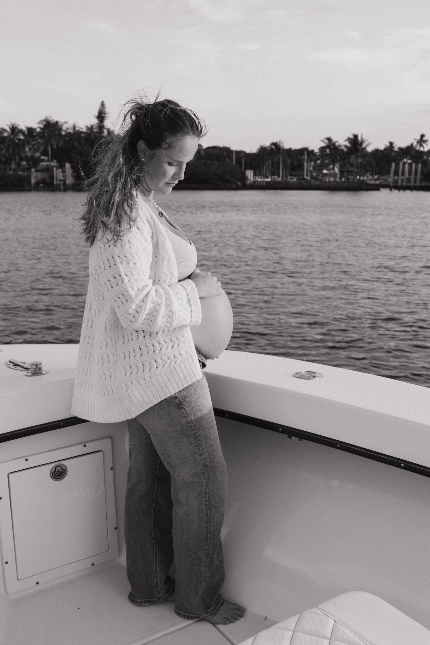 Pregnant woman standing on a boat deck against a waterfront view.