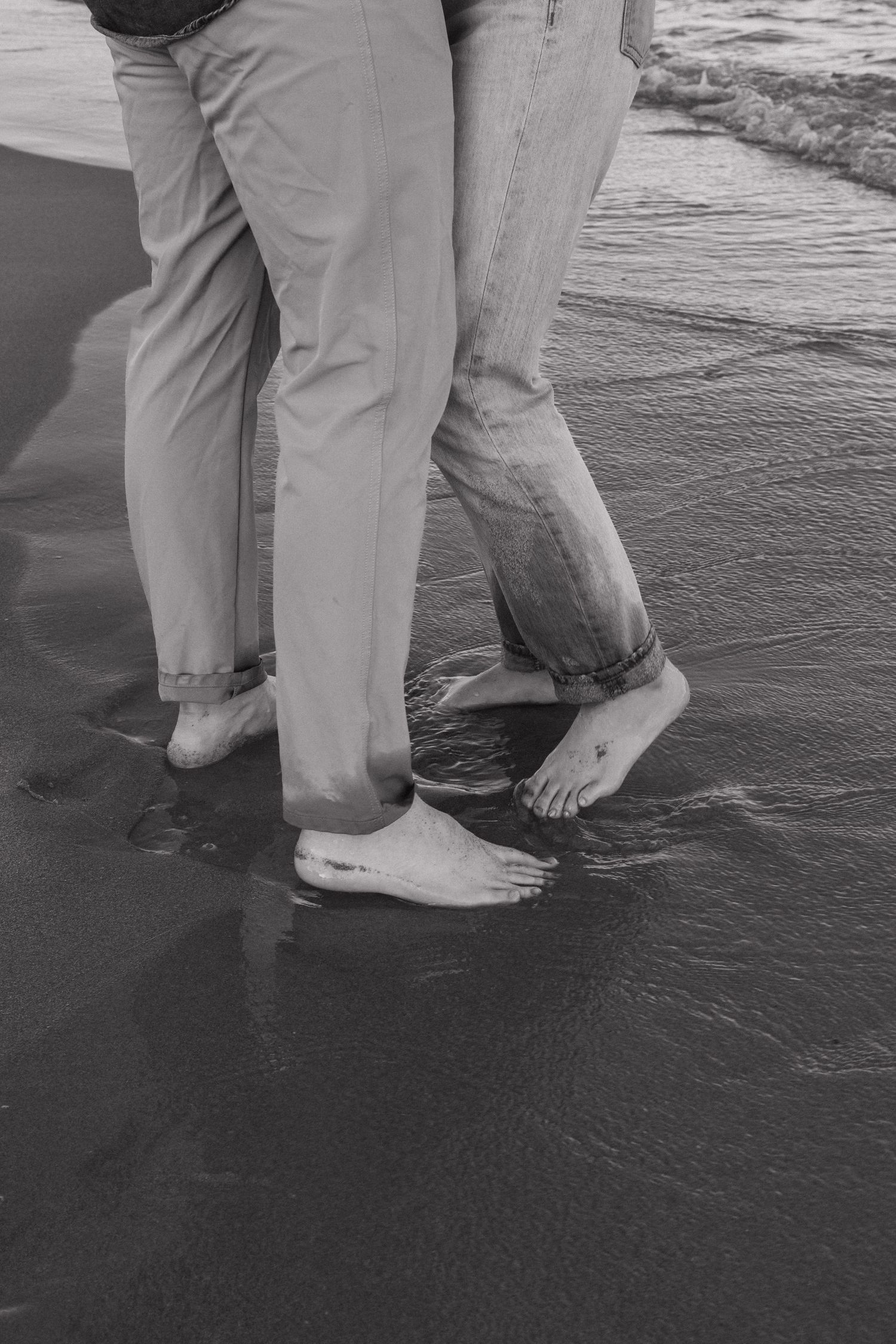 Black and white photo of bare feet in wet sand at the beach.