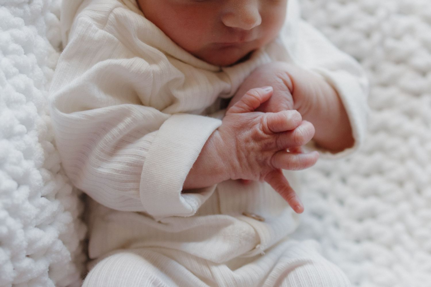 Newborn baby's hands and fingers against white fabric.