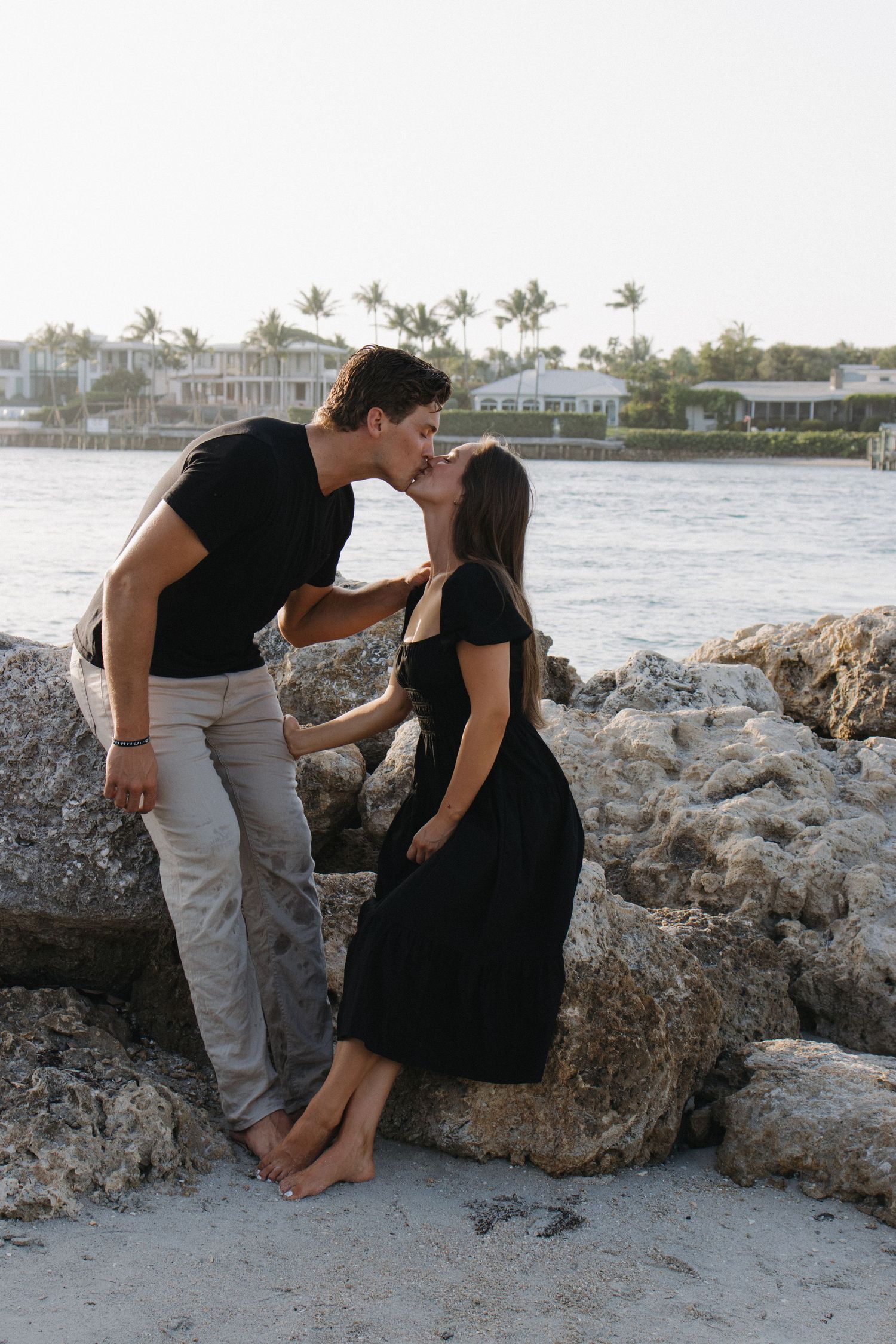A romantic moment captured between a couple on a rocky beach at sunset.