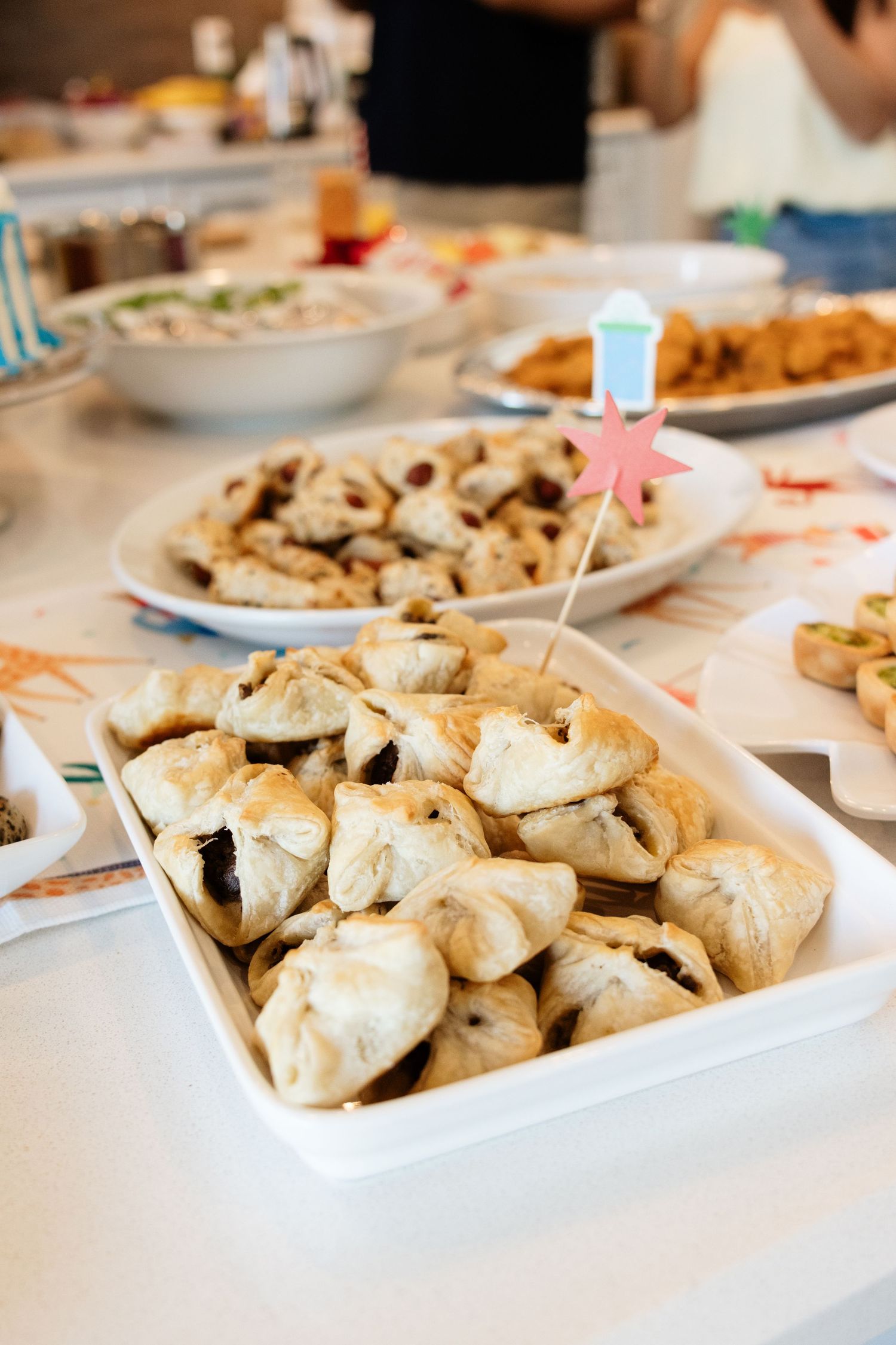 A white dish filled with golden baked hamantaschen pastries on a festive table with other food platters.