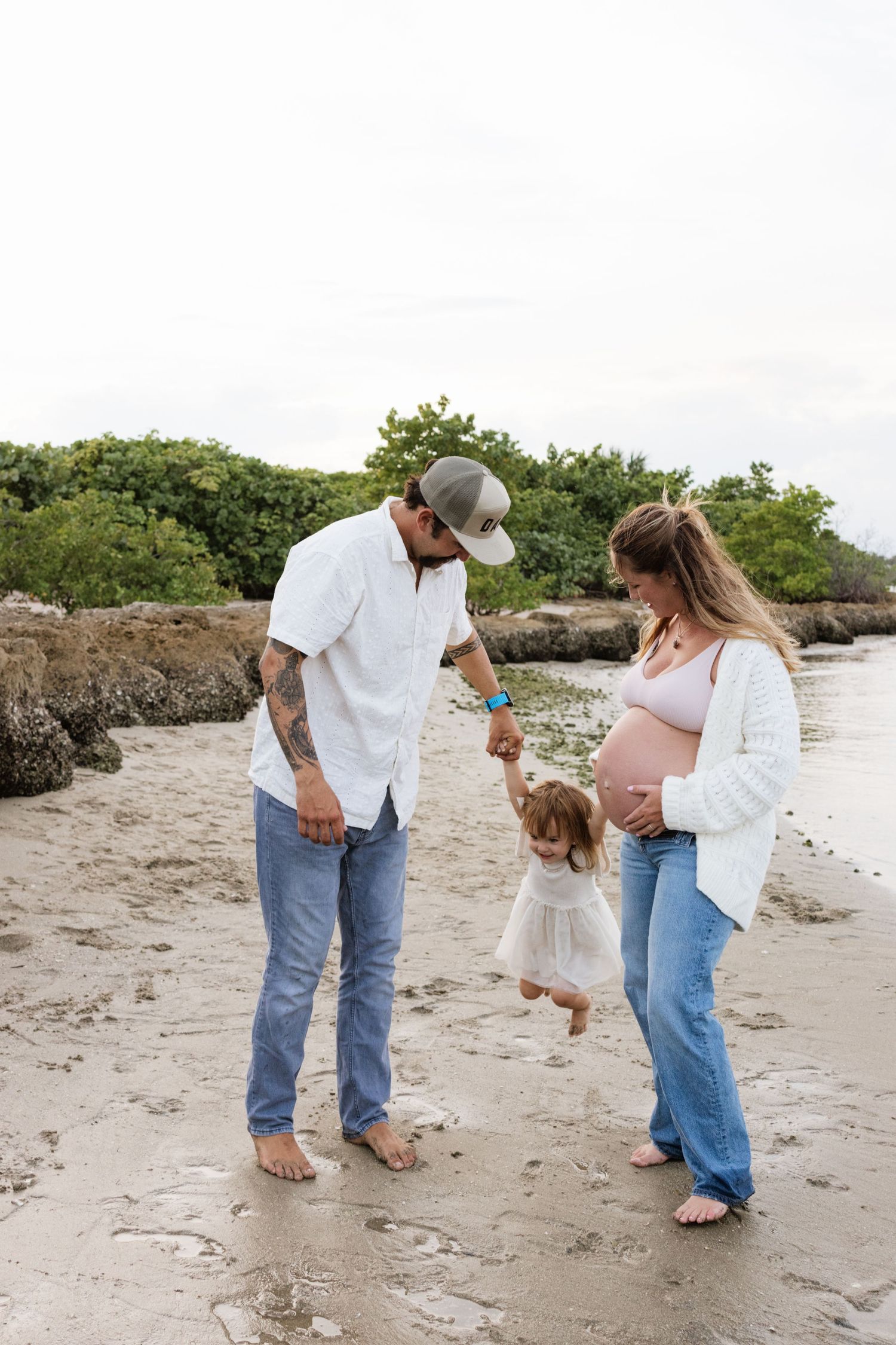 Family playing and walking together on a sandy beach near mangroves.