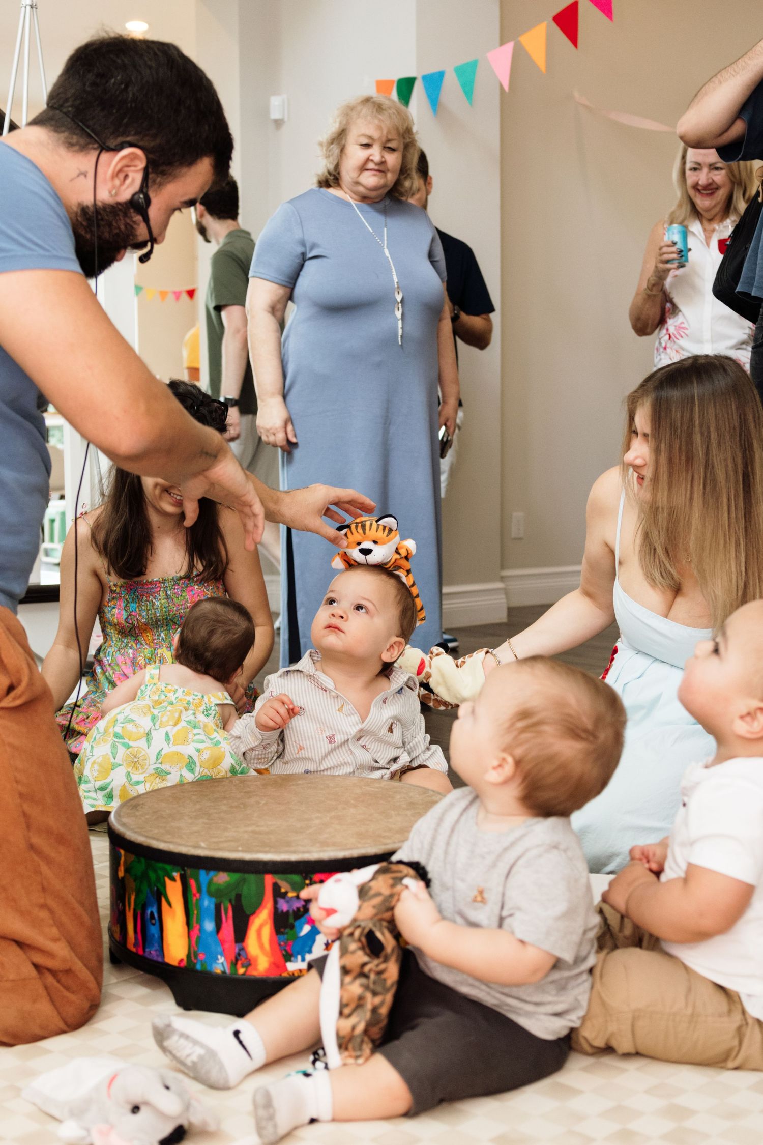 Babies in tiger hats celebrate first birthday party with family gathered around colorful decorations indoors.