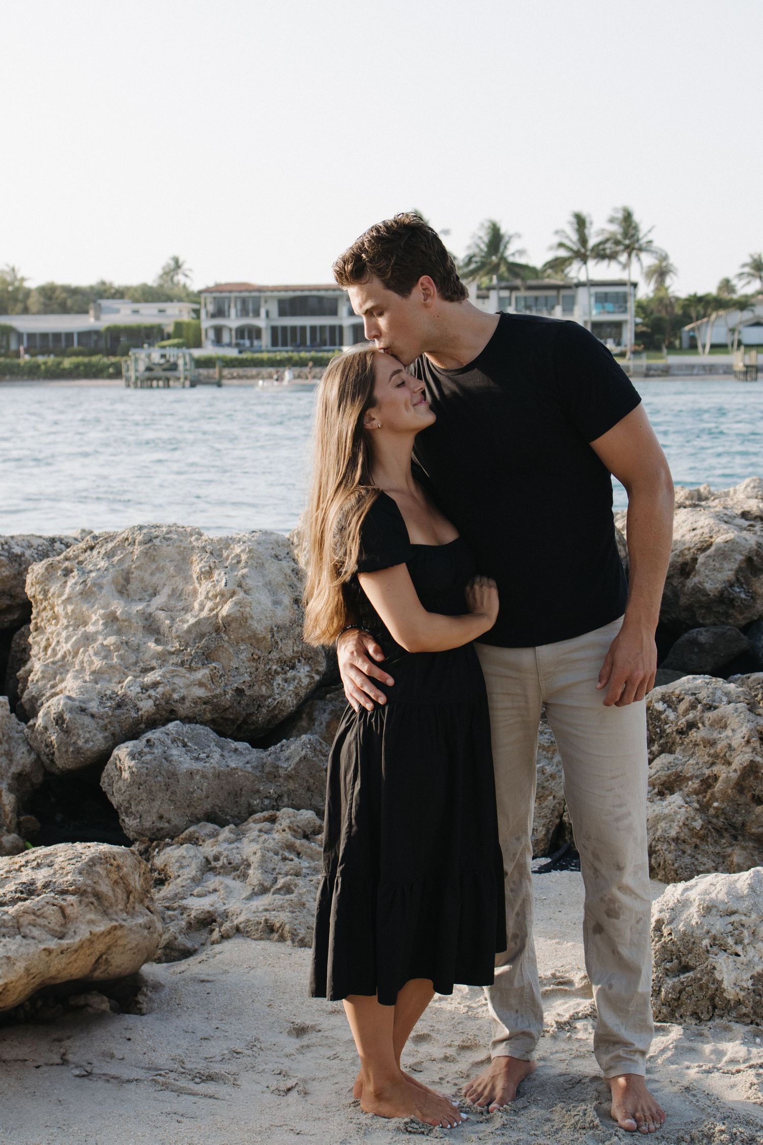 A romantic beach photoshoot with palm trees and waterfront homes in the distance.