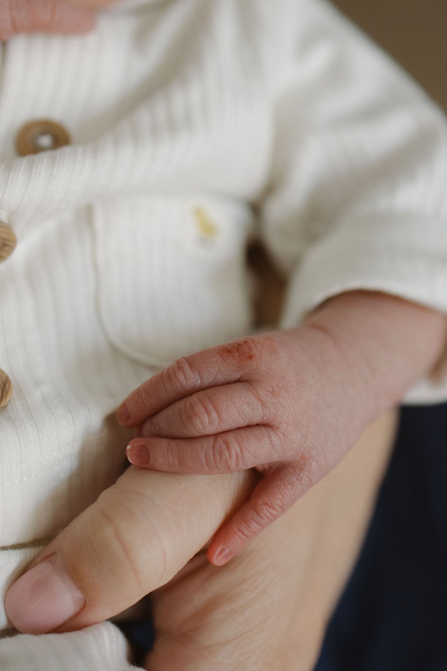 Close-up of small baby hand grasping against white fabric.