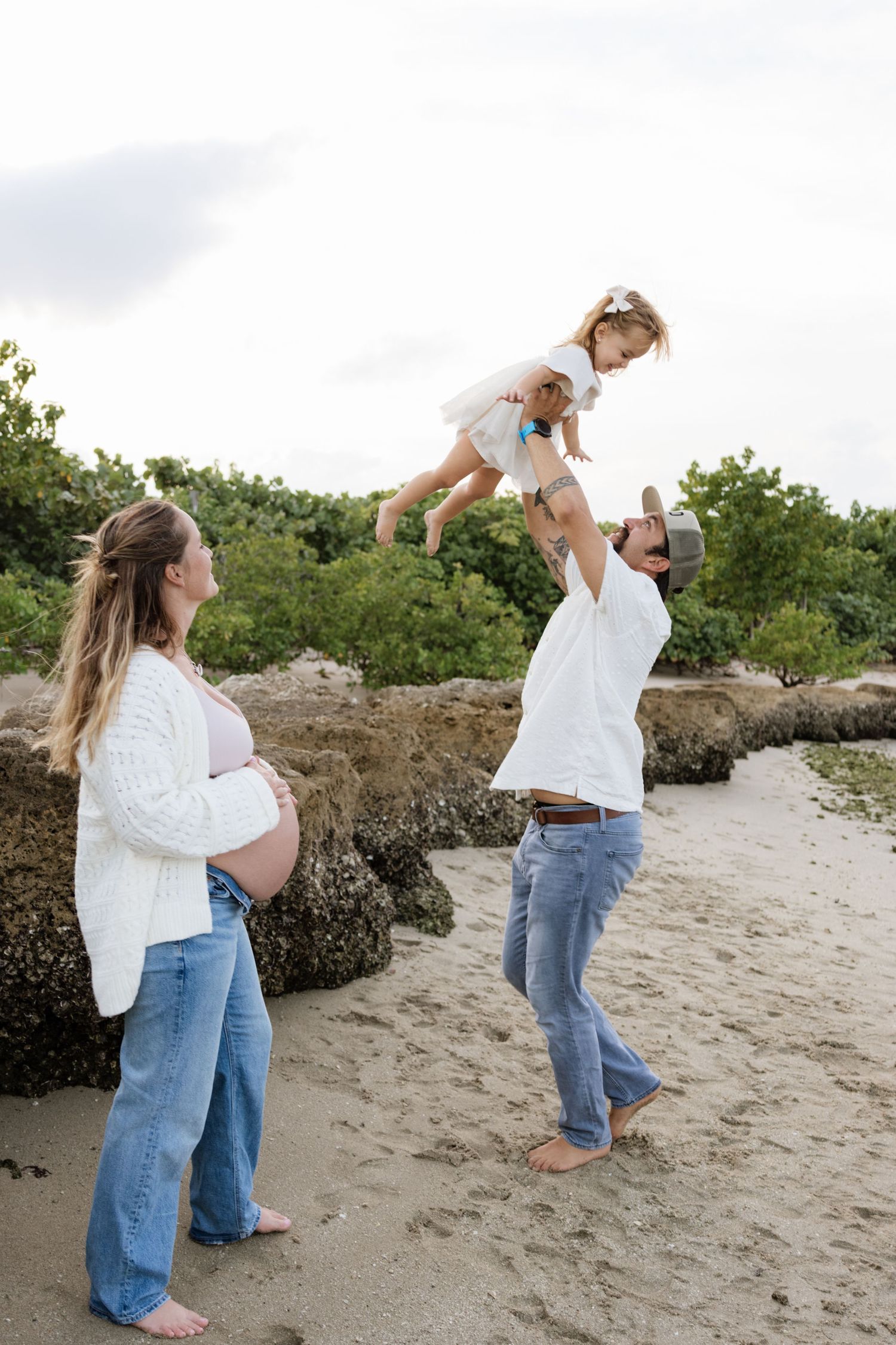 Playful family moments captured on a beach with natural foliage in the background.
