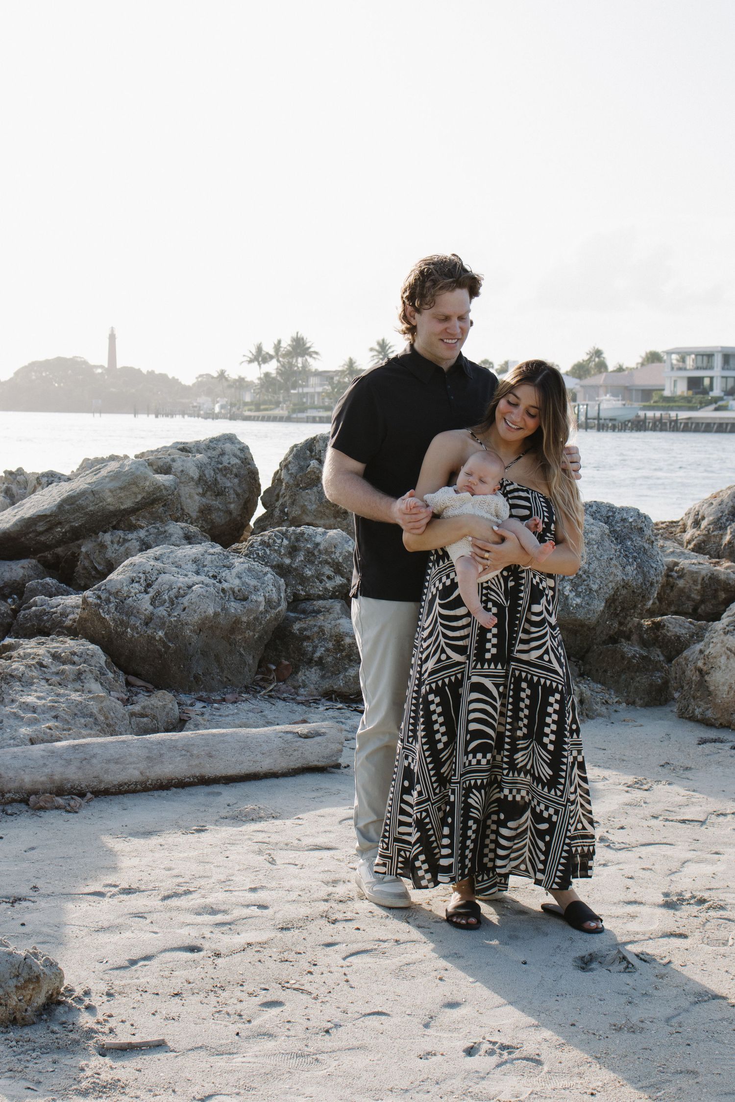 Family portrait session on rocky beach with coastal lighthouse in background.