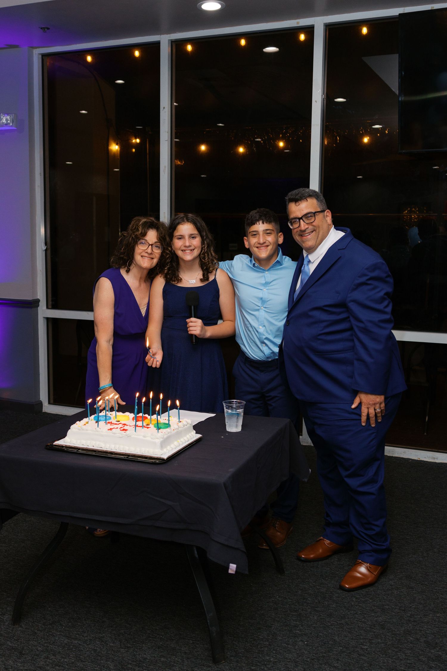 Family of four smiling around a birthday cake with candles at an elegant evening celebration.