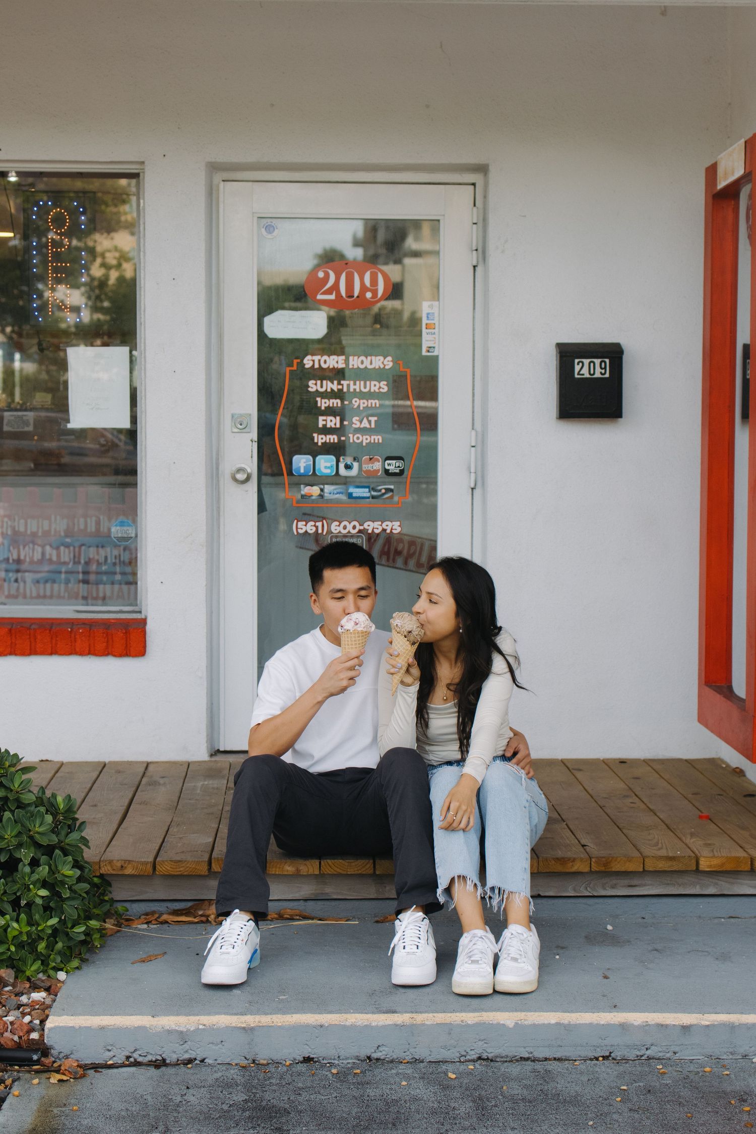 Two people enjoying snacks while sitting on a wooden deck outside a shop.