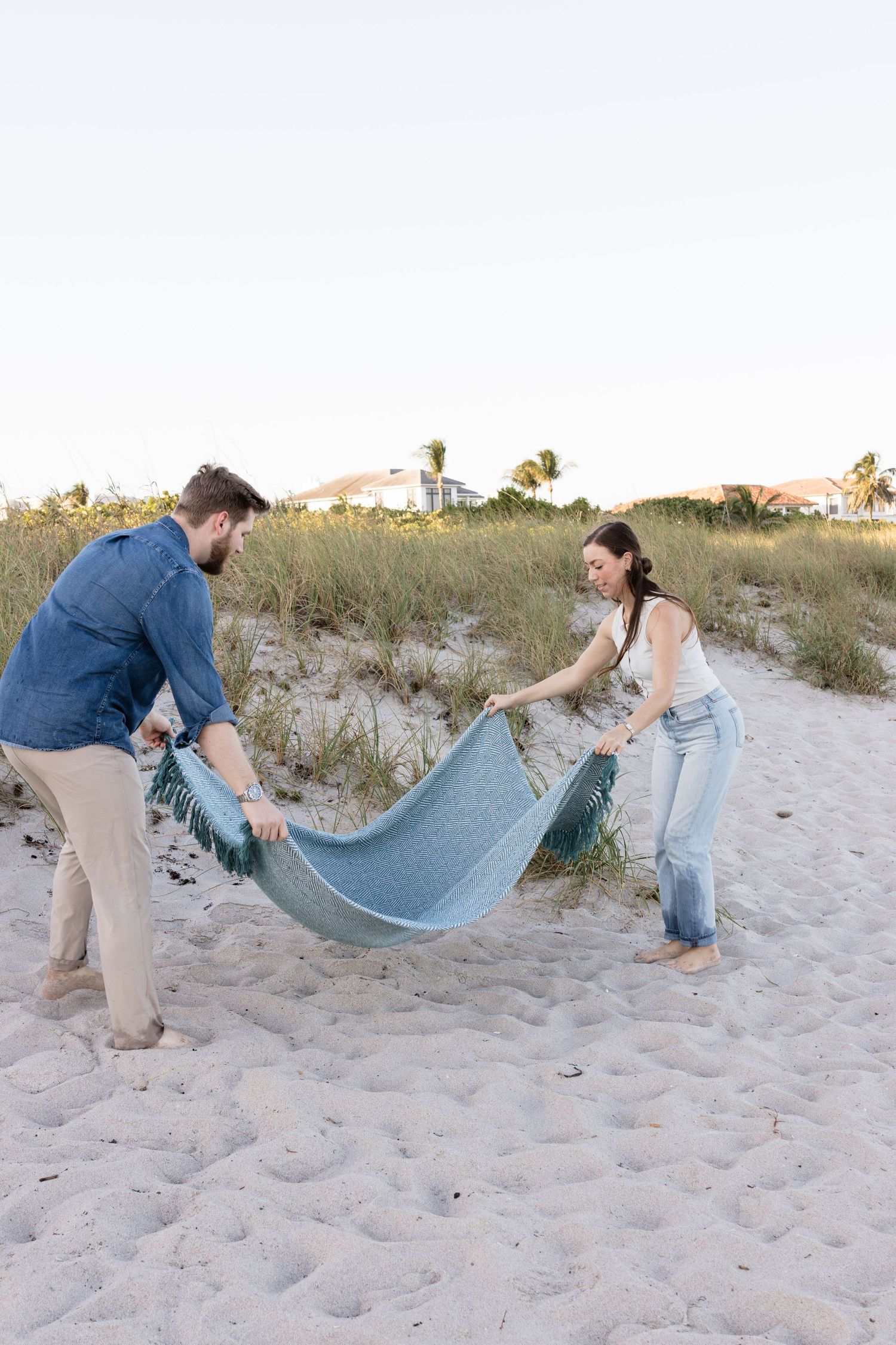 Two people laying out a blue blanket together on beach sand.