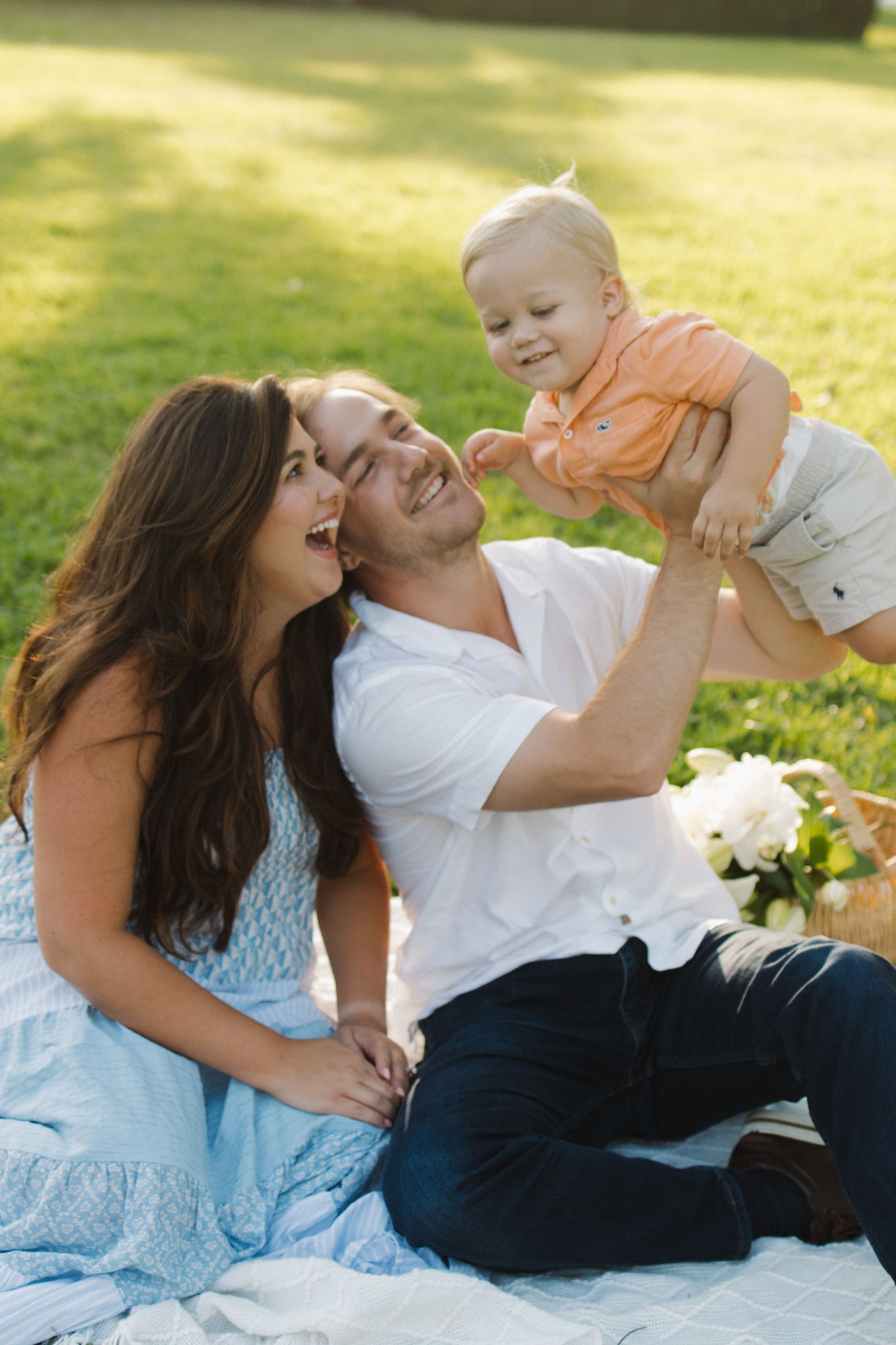 Family laying on blanket in grass sharing playful moments together.