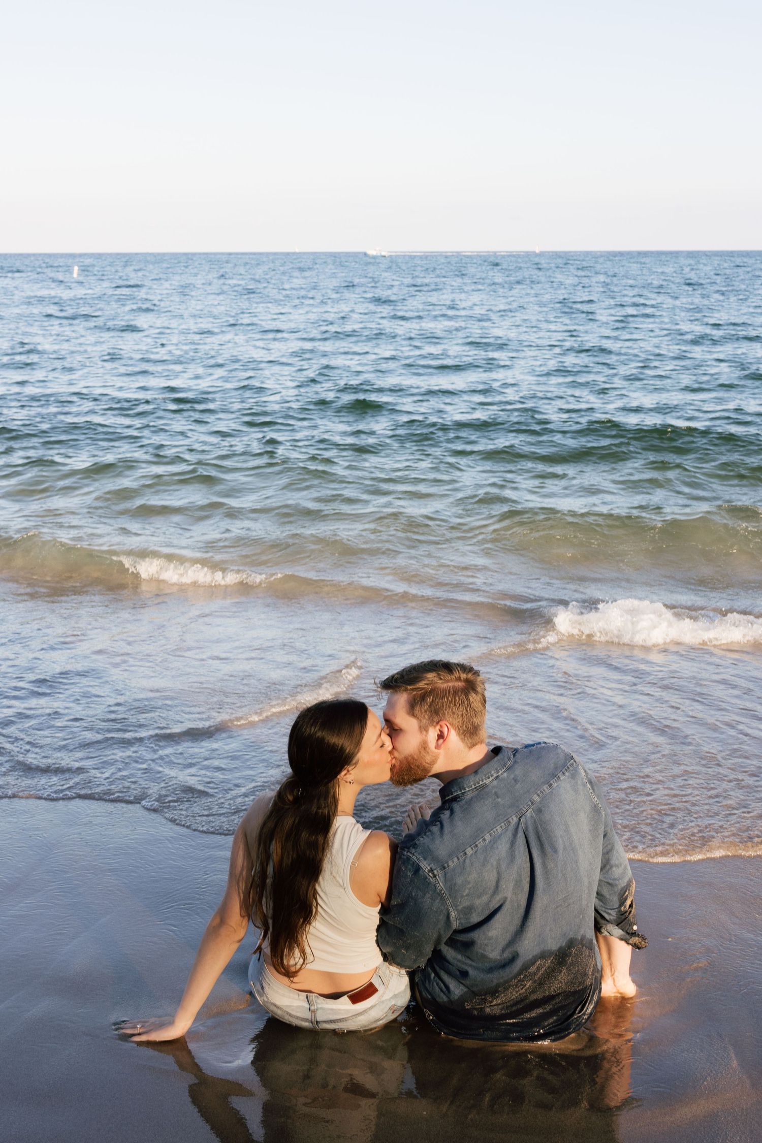 Couple sharing intimate moment at water's edge as waves roll in.