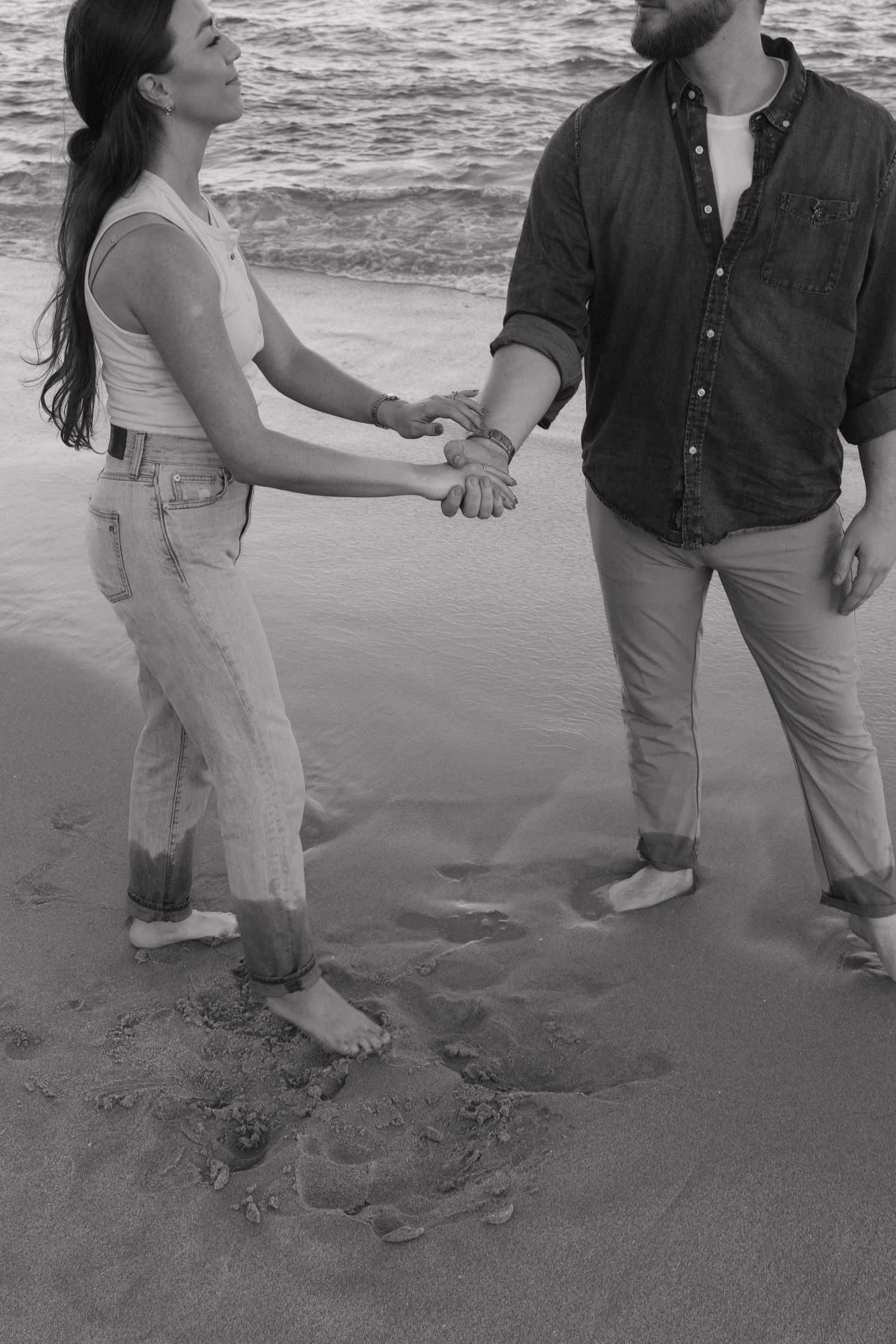 Couple holding hands while walking barefoot on a sandy beach at sunset.