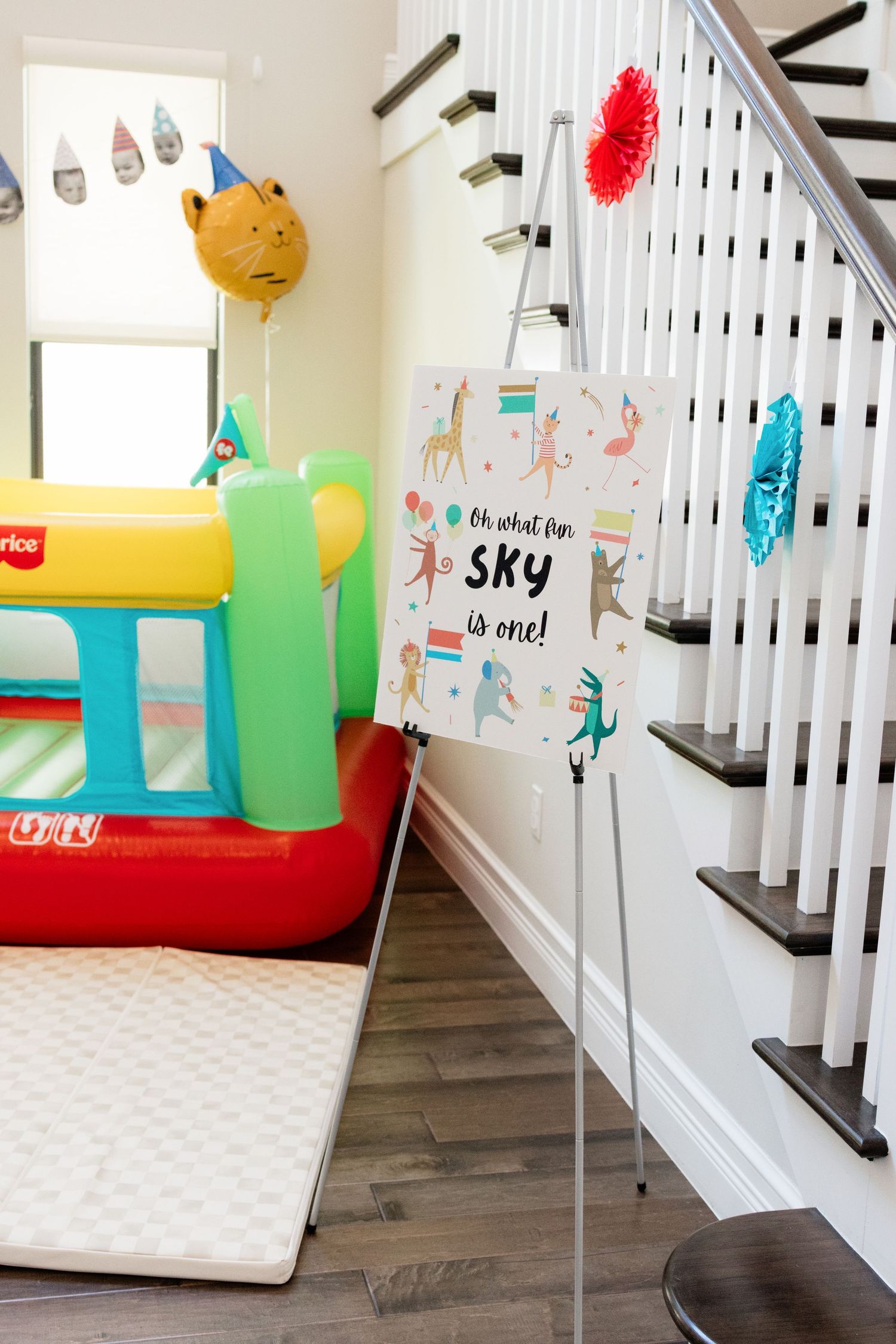 Colorful first birthday party setup with inflatable bounce house, animal balloons, and a sign reading Sky is one.