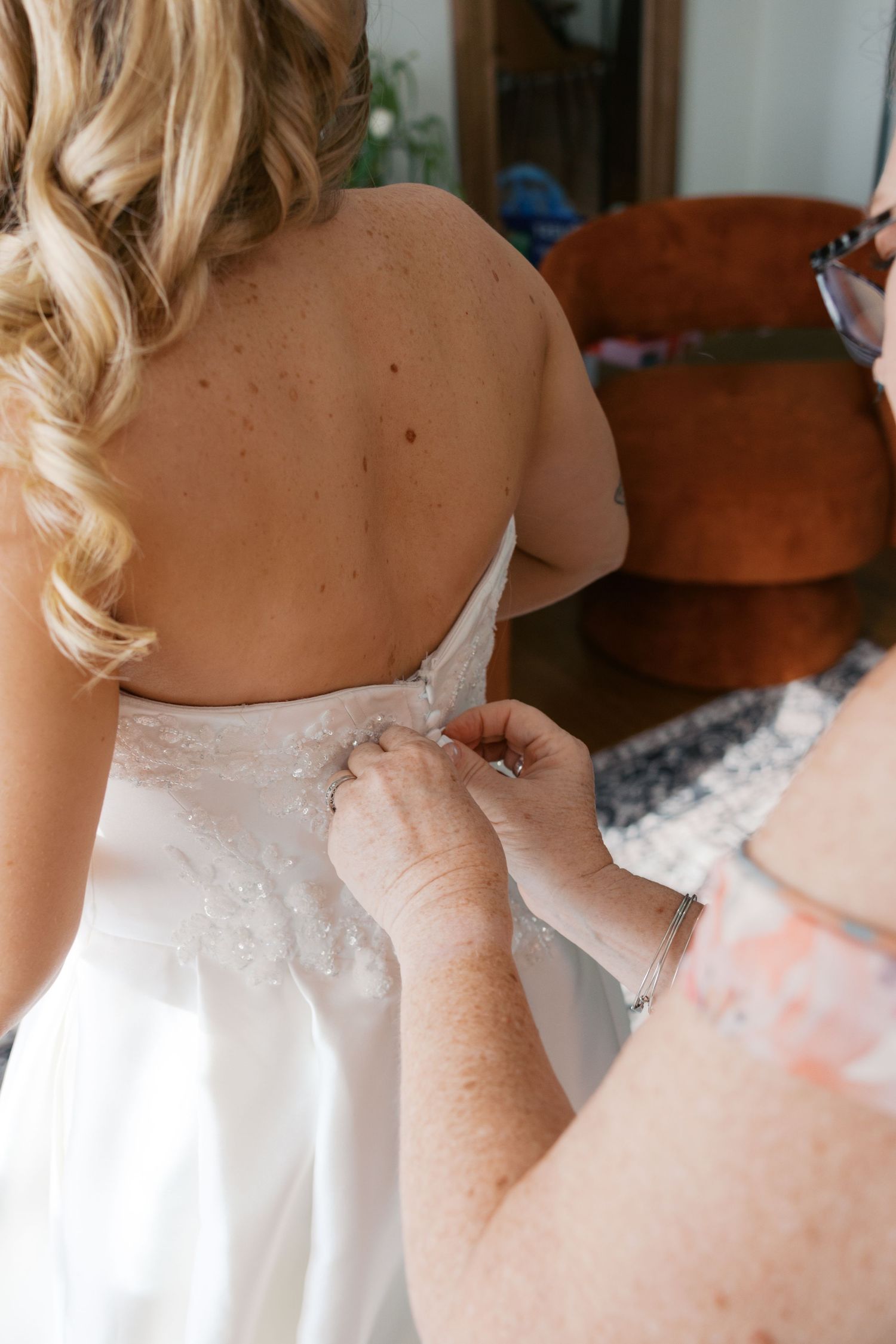 Mother buttoning the back of brides white lace wedding dress before the ceremony.