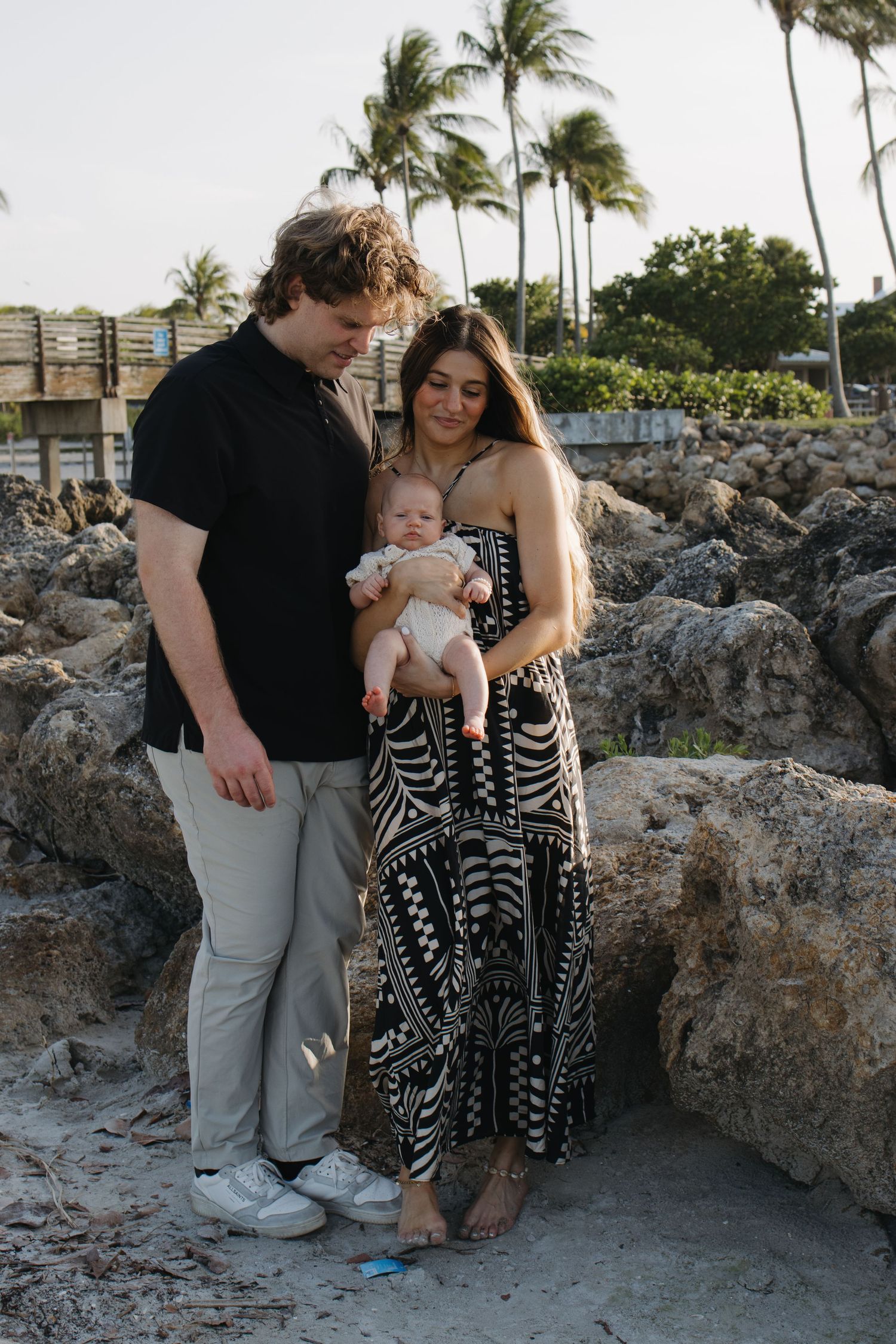 A family in coordinated outfits poses together against coastal rocks at sunset.