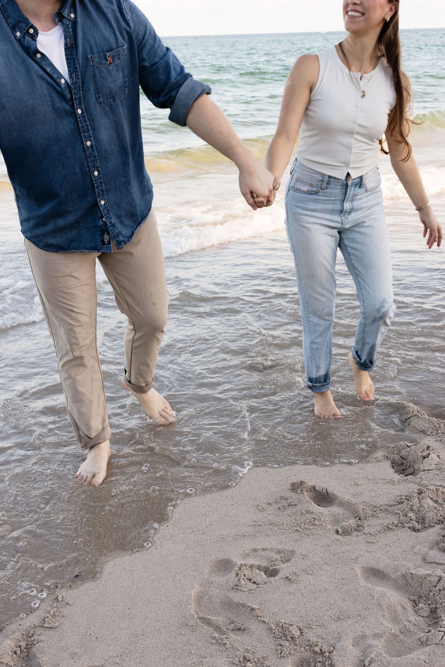 Two people splashing and playing in the shallow ocean water at the beach.
