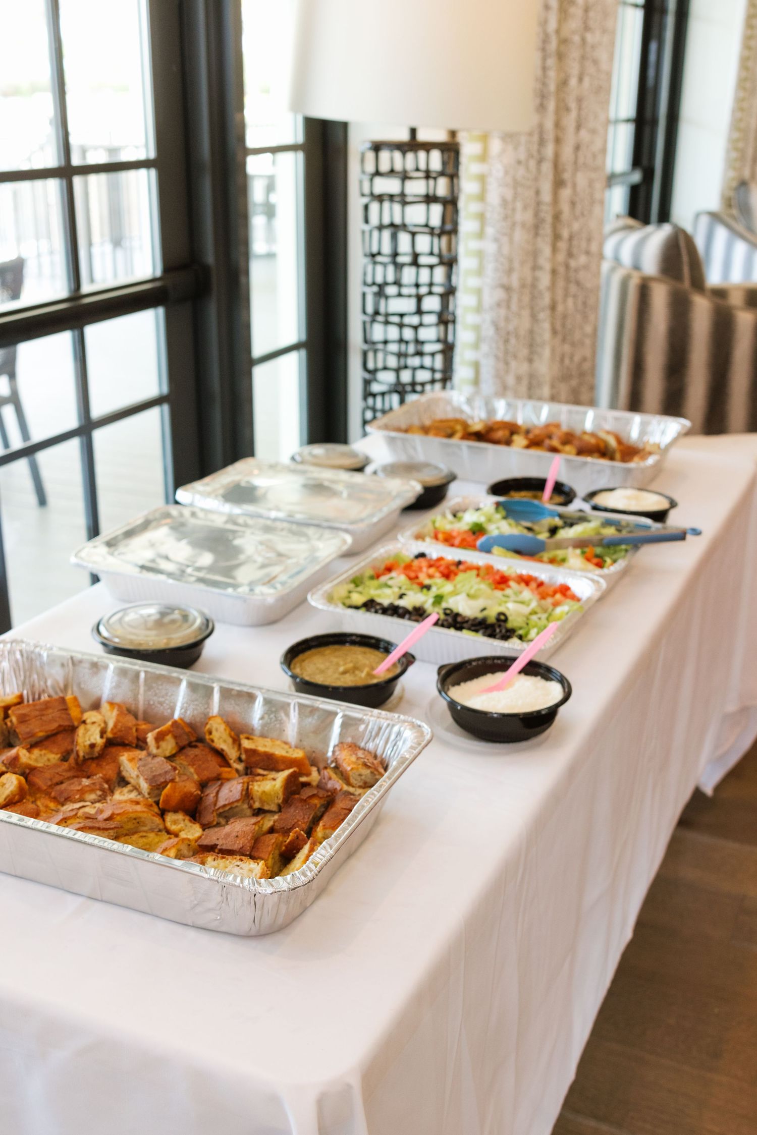 A buffet table with aluminum trays of roasted potatoes, salads, dips, and assorted dishes set up for a catered event.