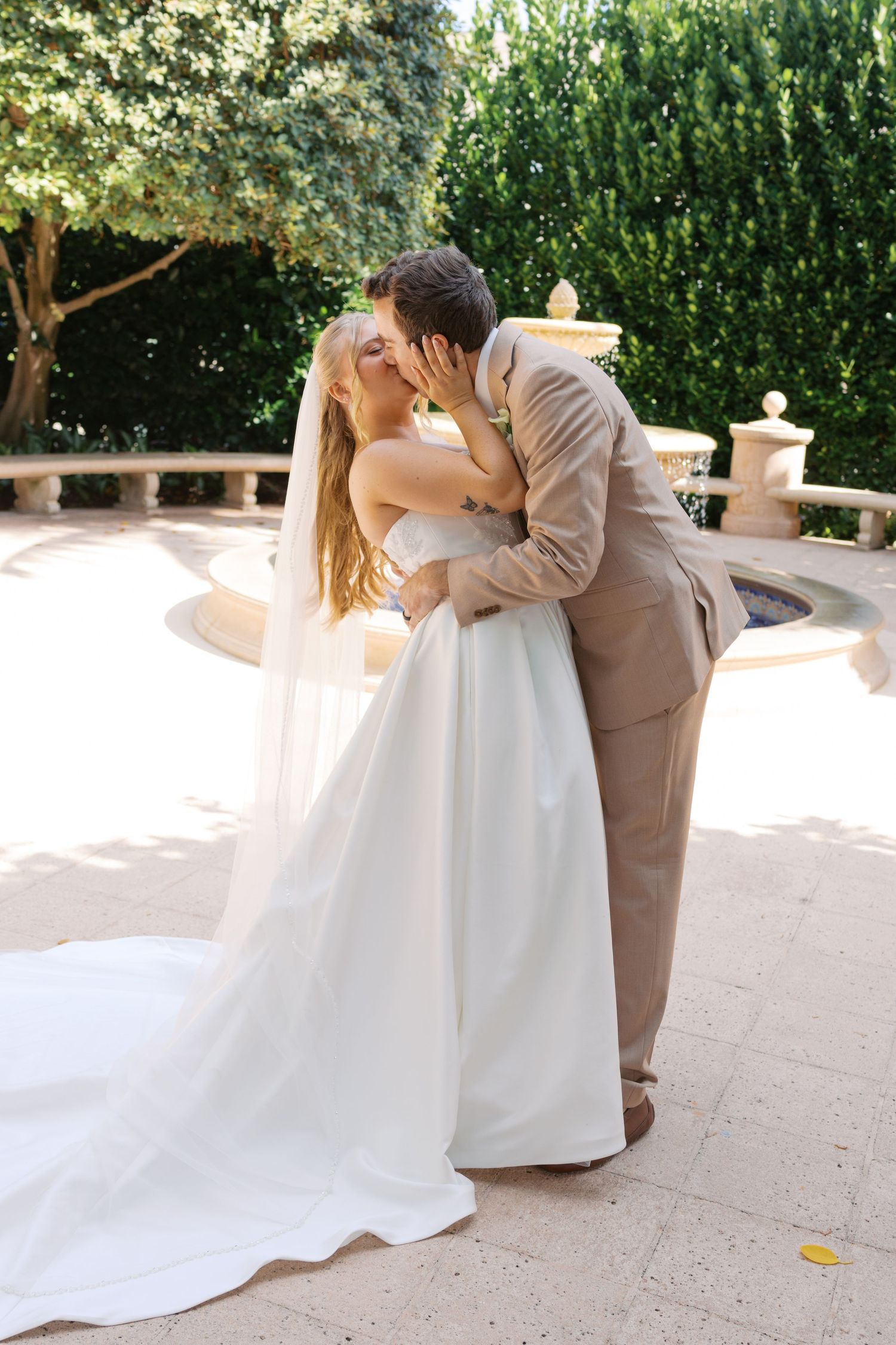 Bride and groom share a romantic kiss outdoors in a garden setting on their wedding day.