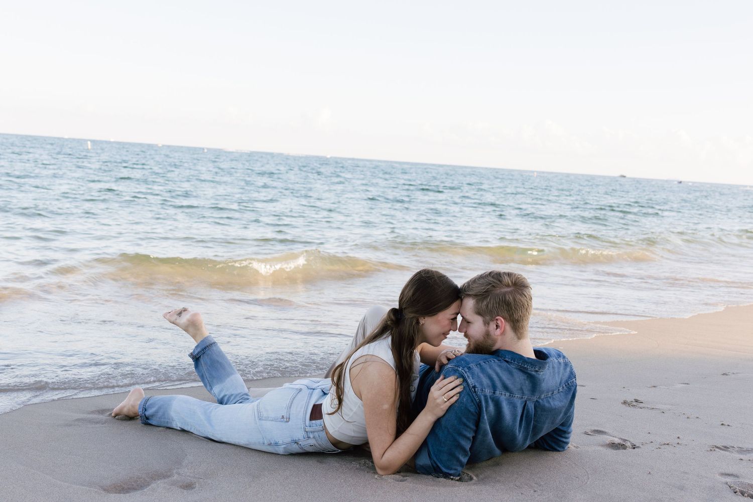 Couple in casual attire sharing tender moment on sandy beach.