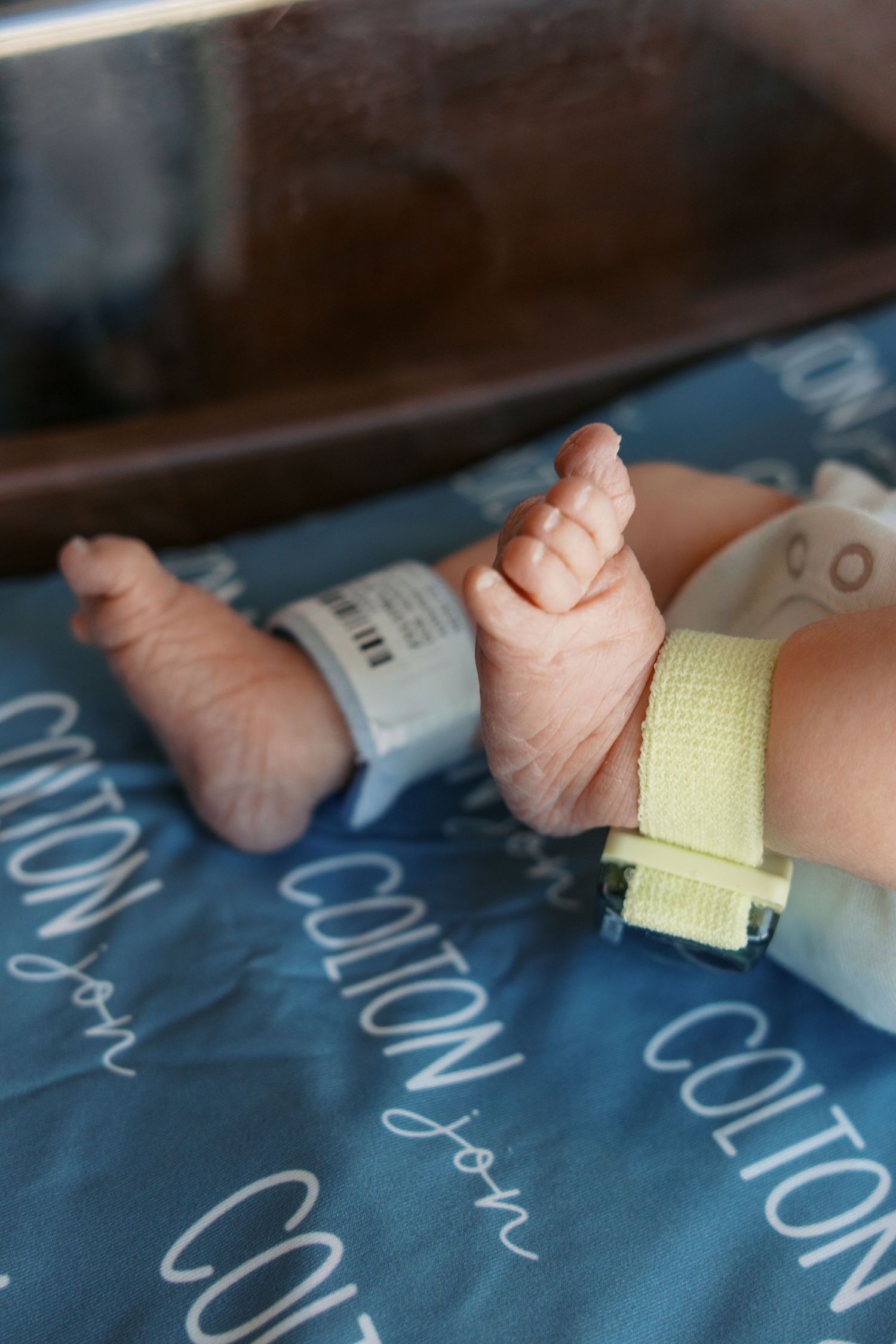 Newborn baby feet with hospital ID bracelets resting on a personalized blue blanket named Colton.
