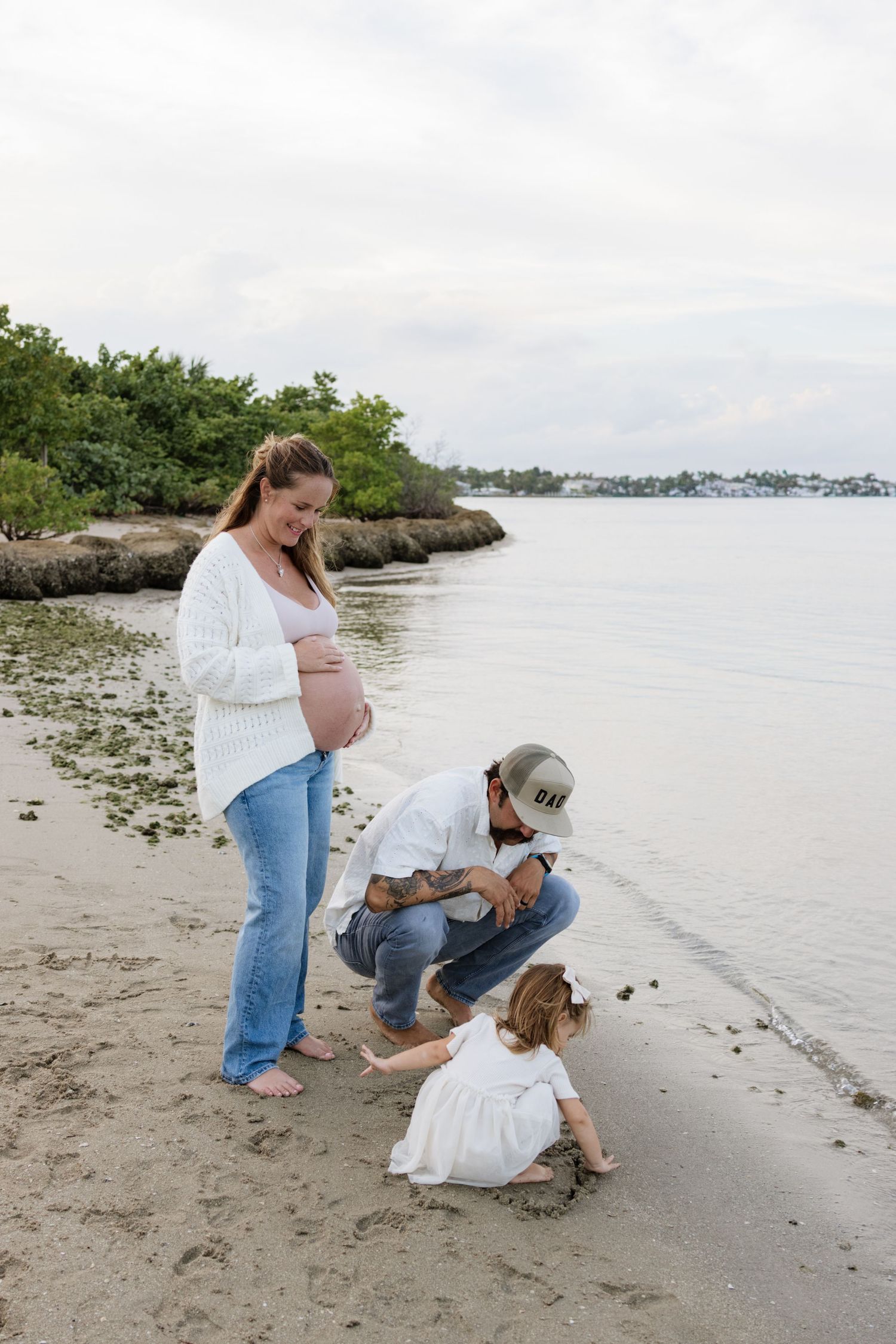 Family members explore and play along a sandy shoreline near the water.