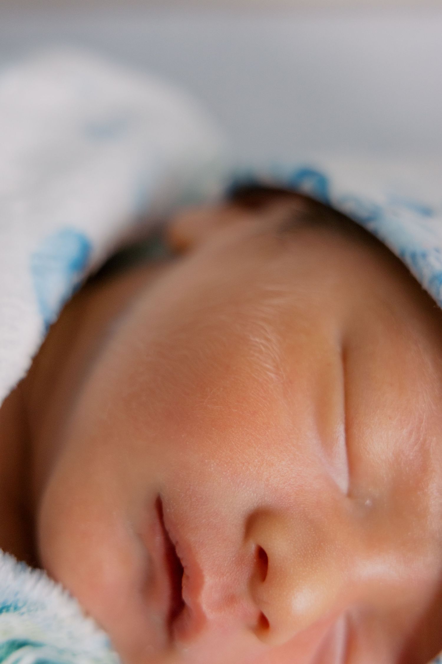 Close-up of a sleeping newborn baby with closed eyes, wearing a blue hat, peaceful expression.