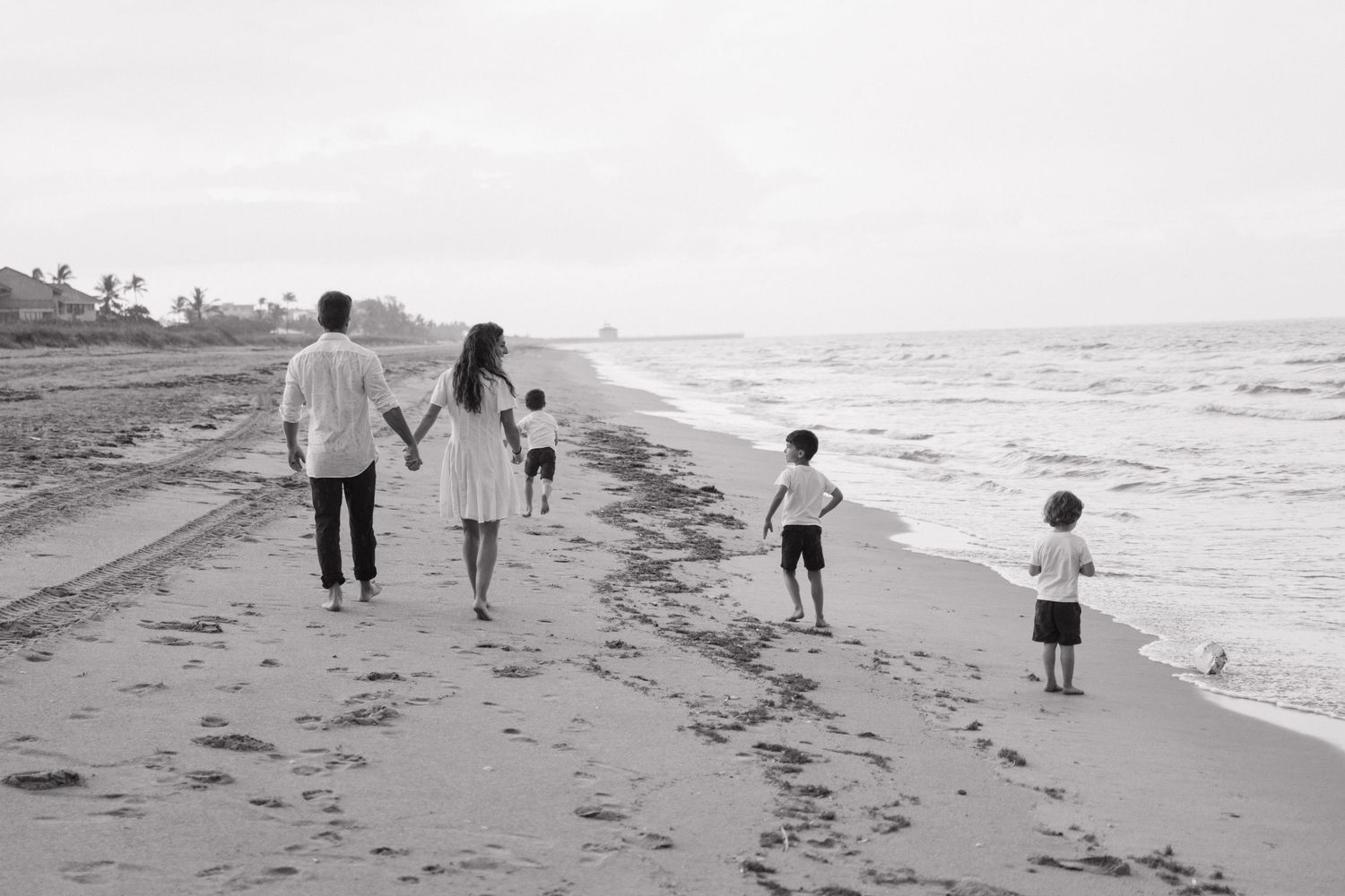 Family walking together along beach shoreline in black and white.