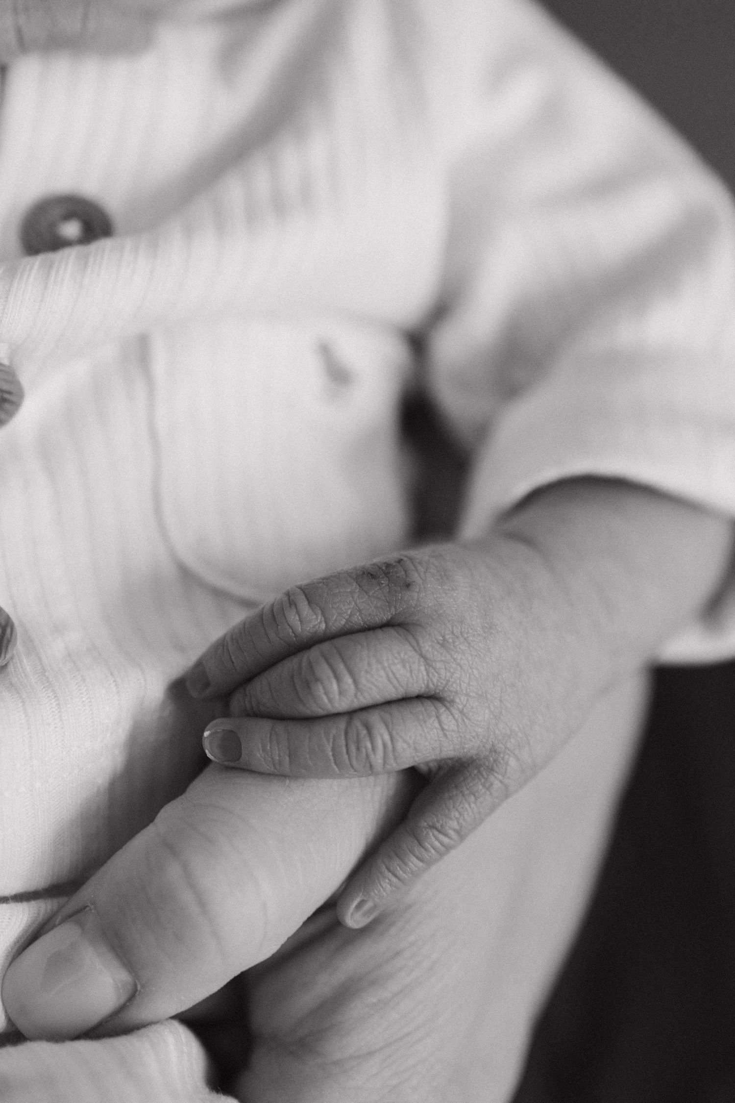 Black and white close-up of infant's hand against light fabric.