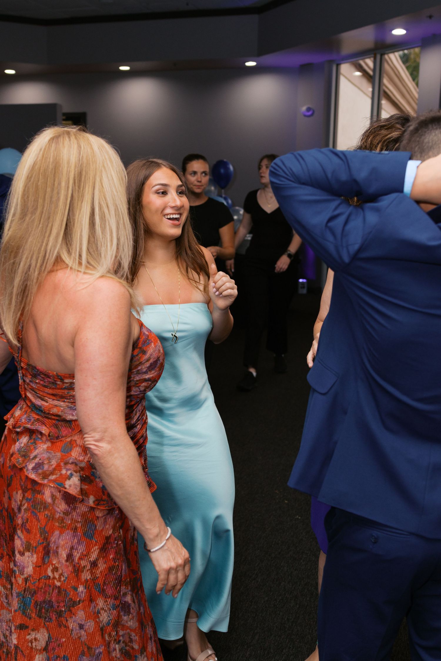 People dancing at a formal event, woman in light blue satin dress smiling, others in floral and blue suit attire.