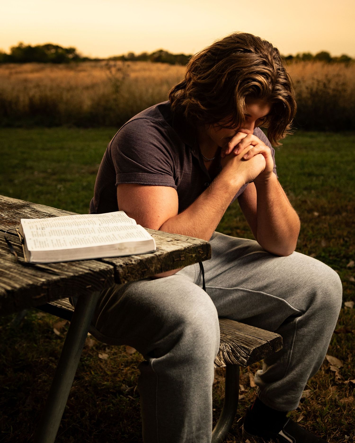 Person sits contemplatively on wooden bench with book during golden hour.