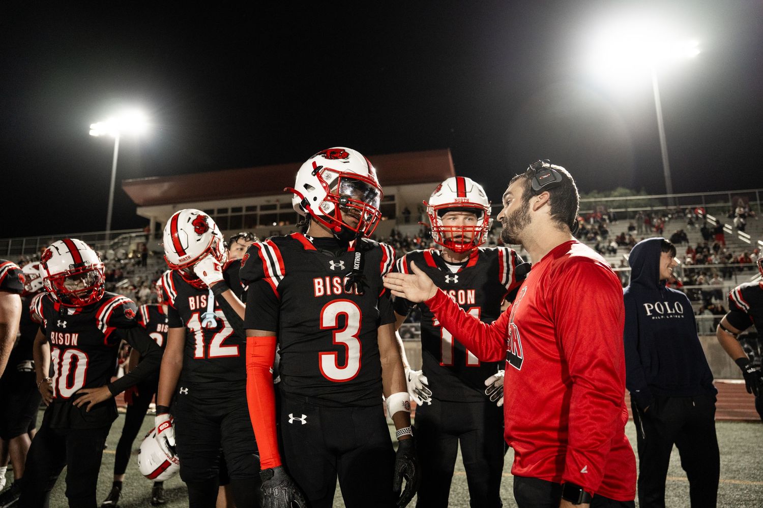 Football team celebrating victory under stadium lights at night.