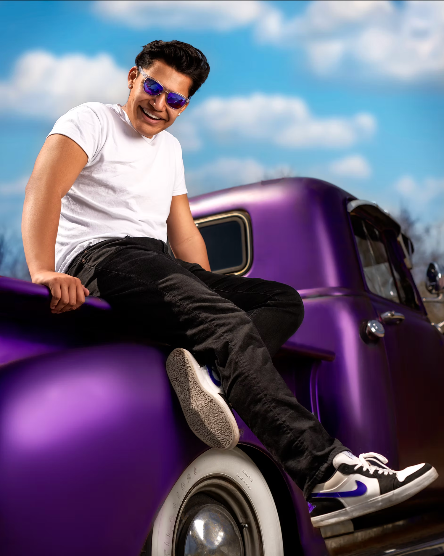 Person lounging on purple vintage car under blue sky.