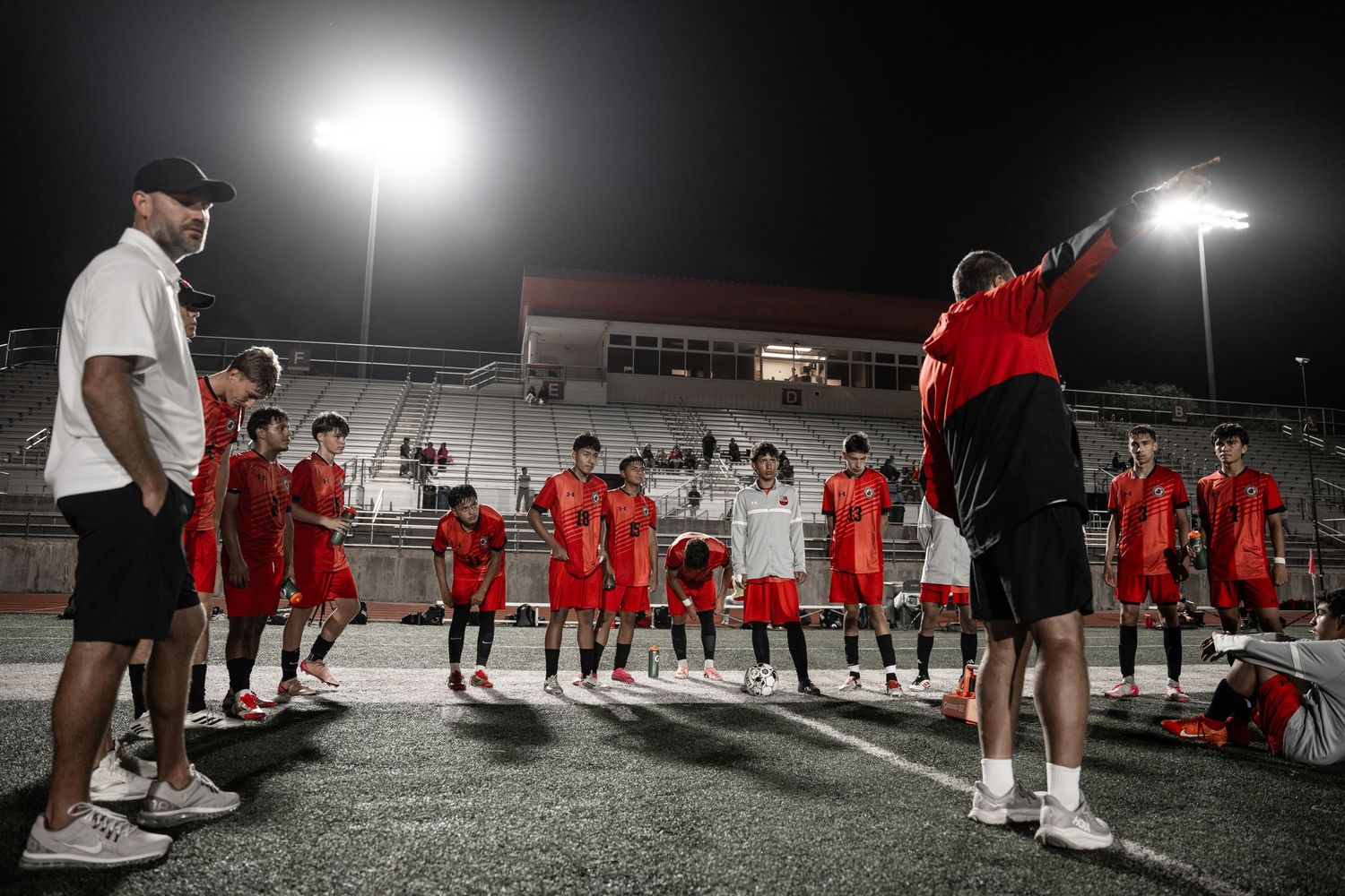 Soccer players gather under stadium lights during nighttime practice session.