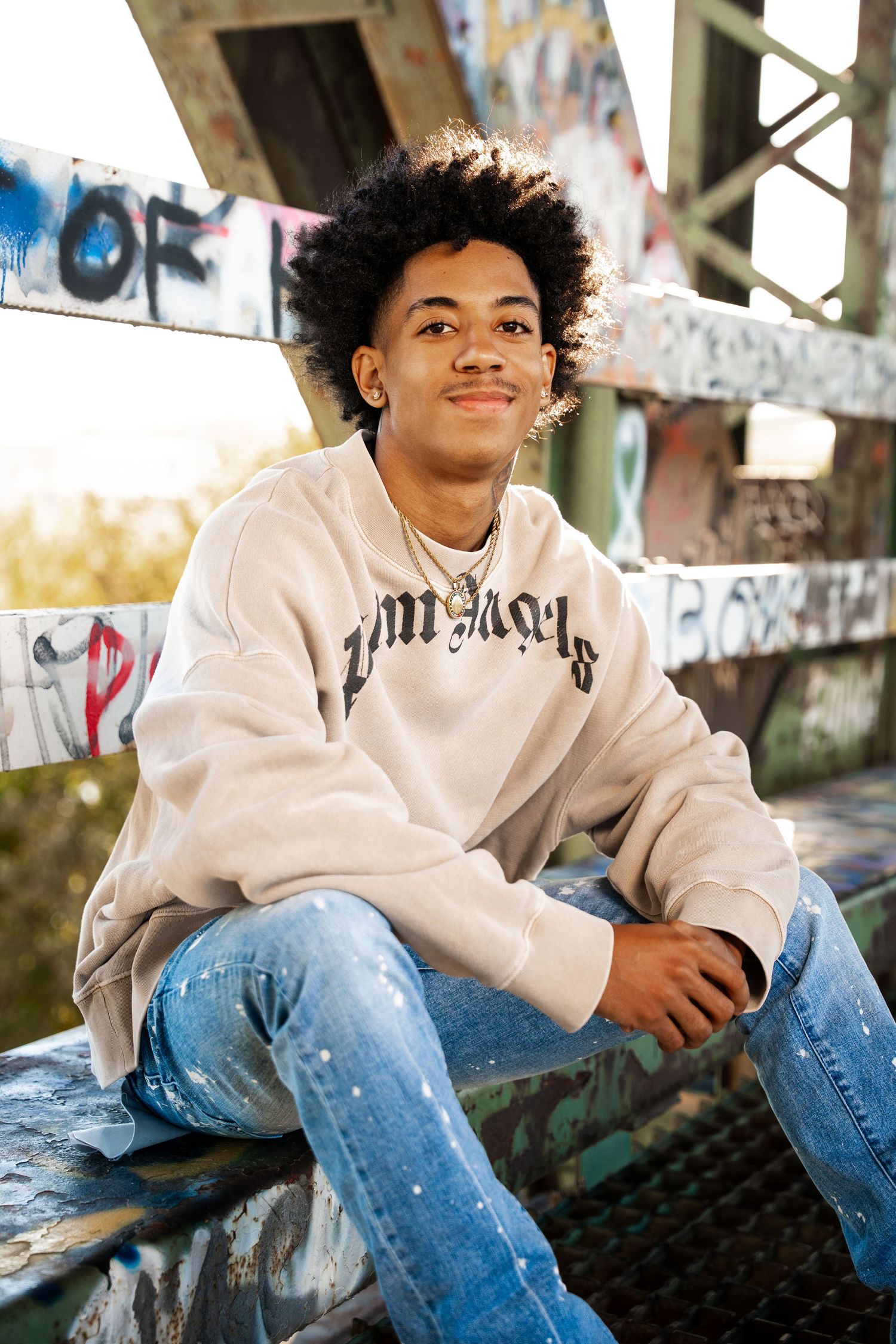 Person in white hoodie and distressed jeans sitting casually on urban structure.