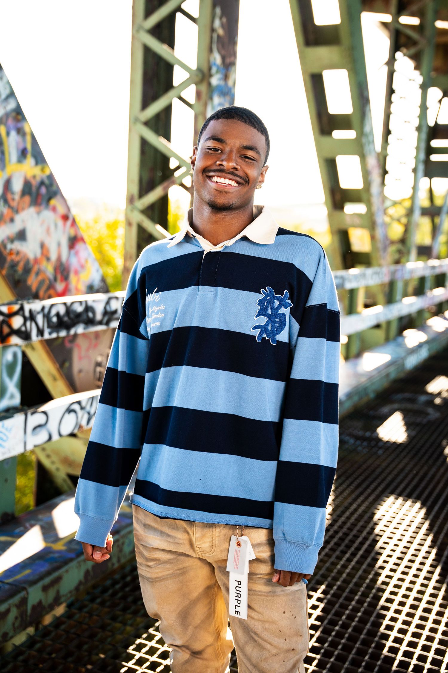 Young person wearing a light blue and navy striped polo shirt smiling outdoors.