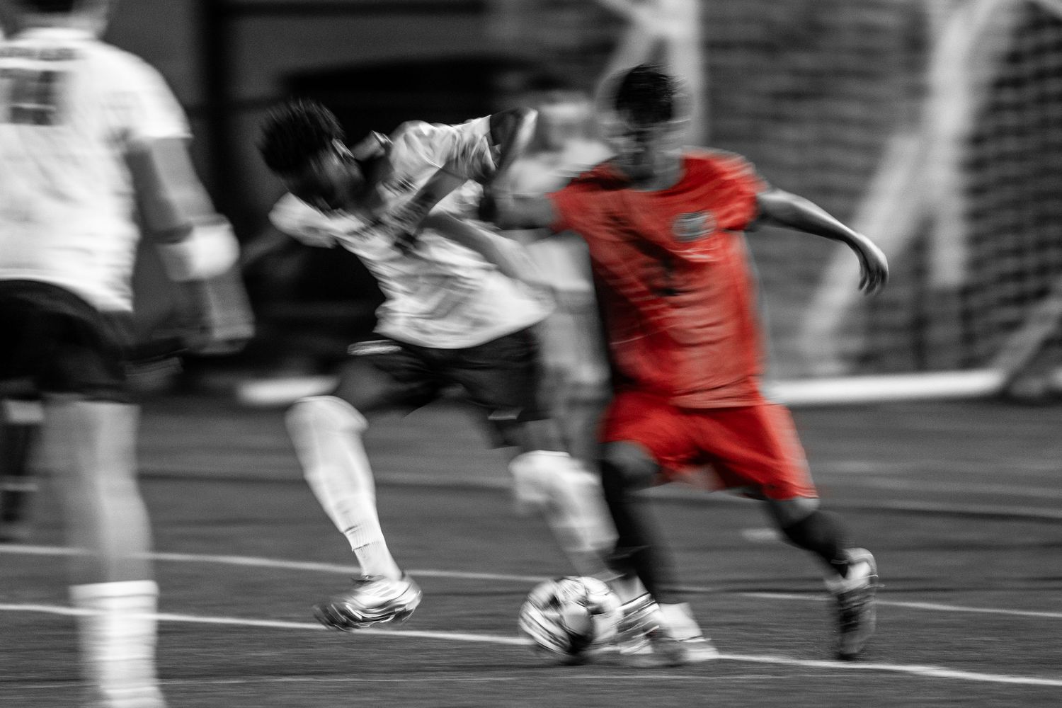 Motion-blurred black and white image of athletes playing soccer on field.