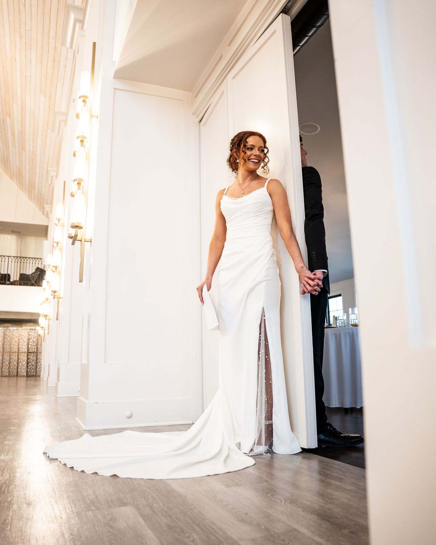 A bride in a flowing white wedding dress twirls gracefully in a bright indoor space with wooden floors.