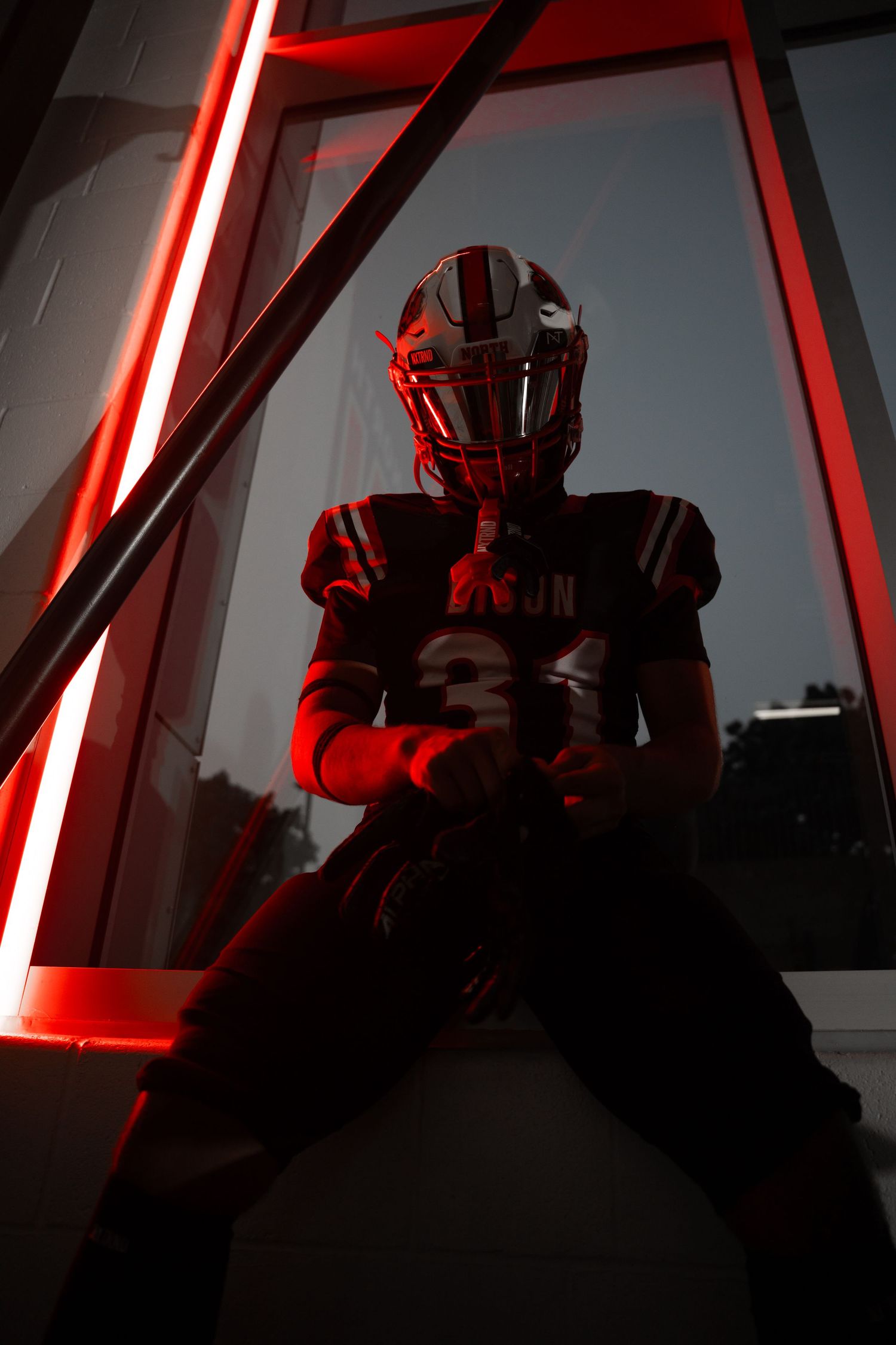 Dramatic red-lit silhouette of football player in helmet against geometric background.