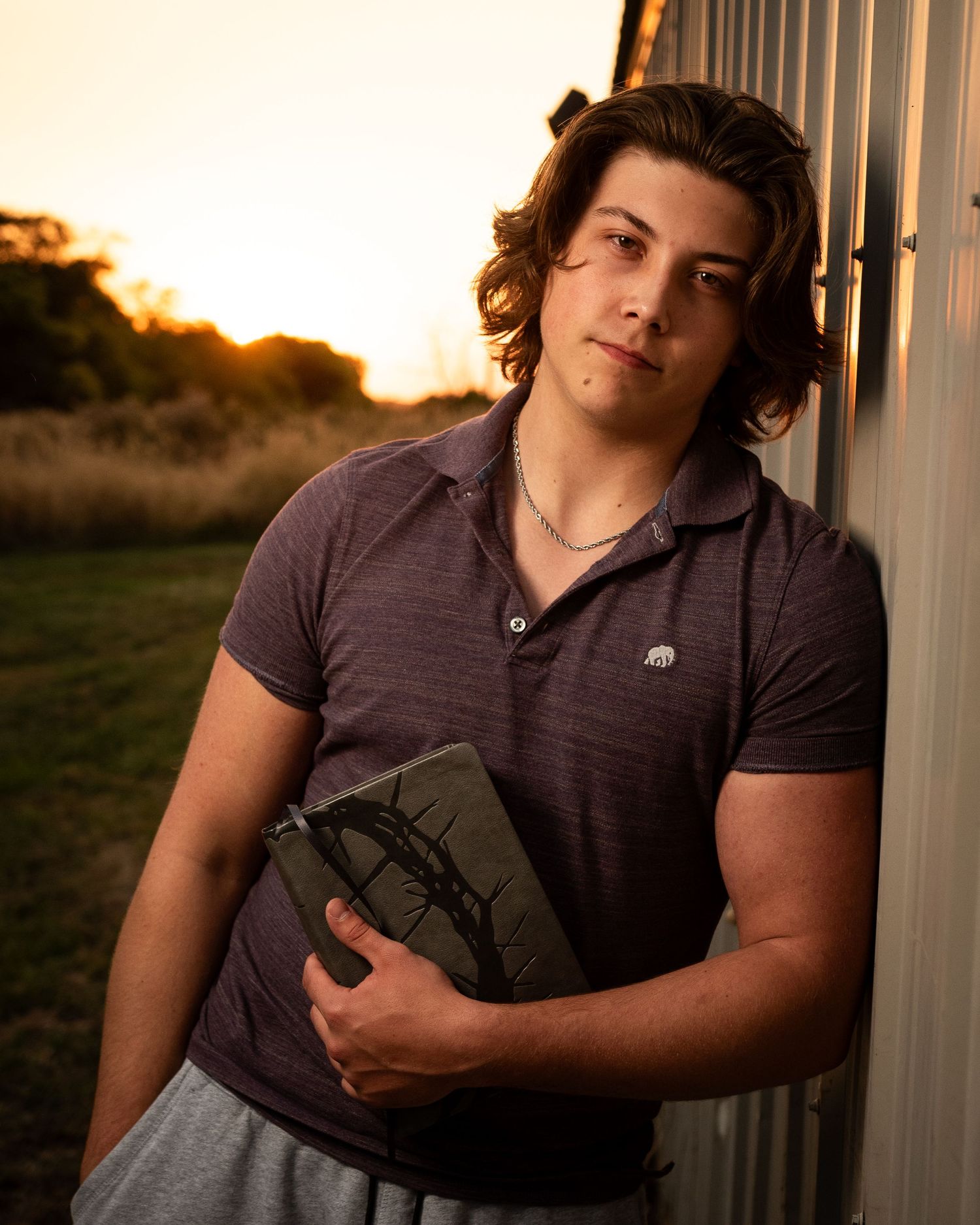 Portrait session against rustic building during sunset with moody lighting.