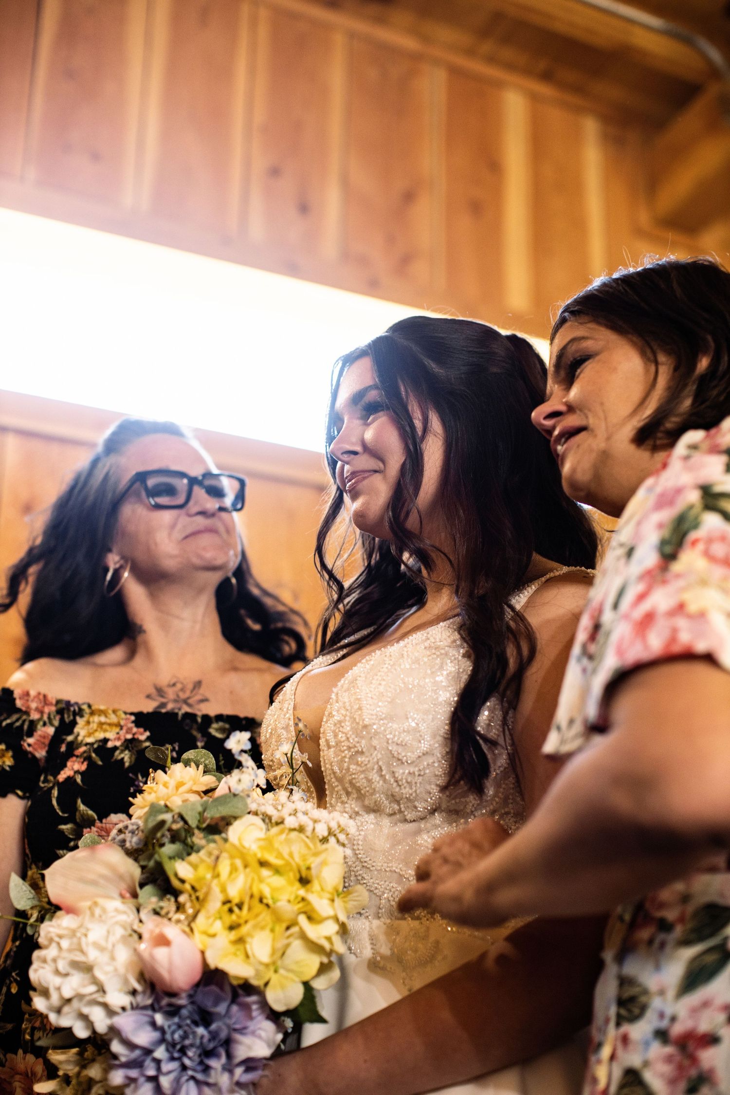Bride smiling with bouquet surrounded by family in a warmly lit wooden venue.