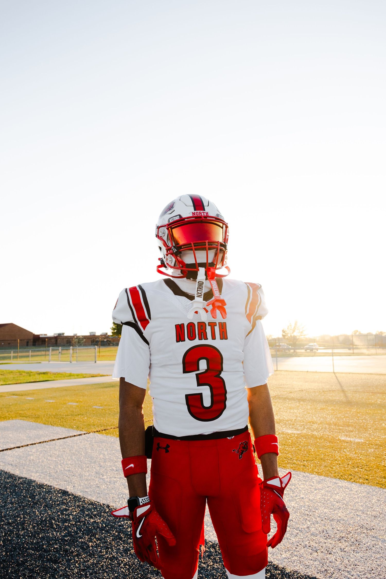 Football players in red and white uniforms stand together on field at sunset.